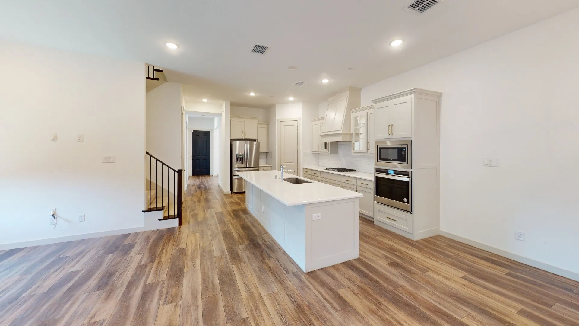 Open-concept kitchen with a large central island, white cabinetry, integrated stainless steel appliances, and wood-finish flooring