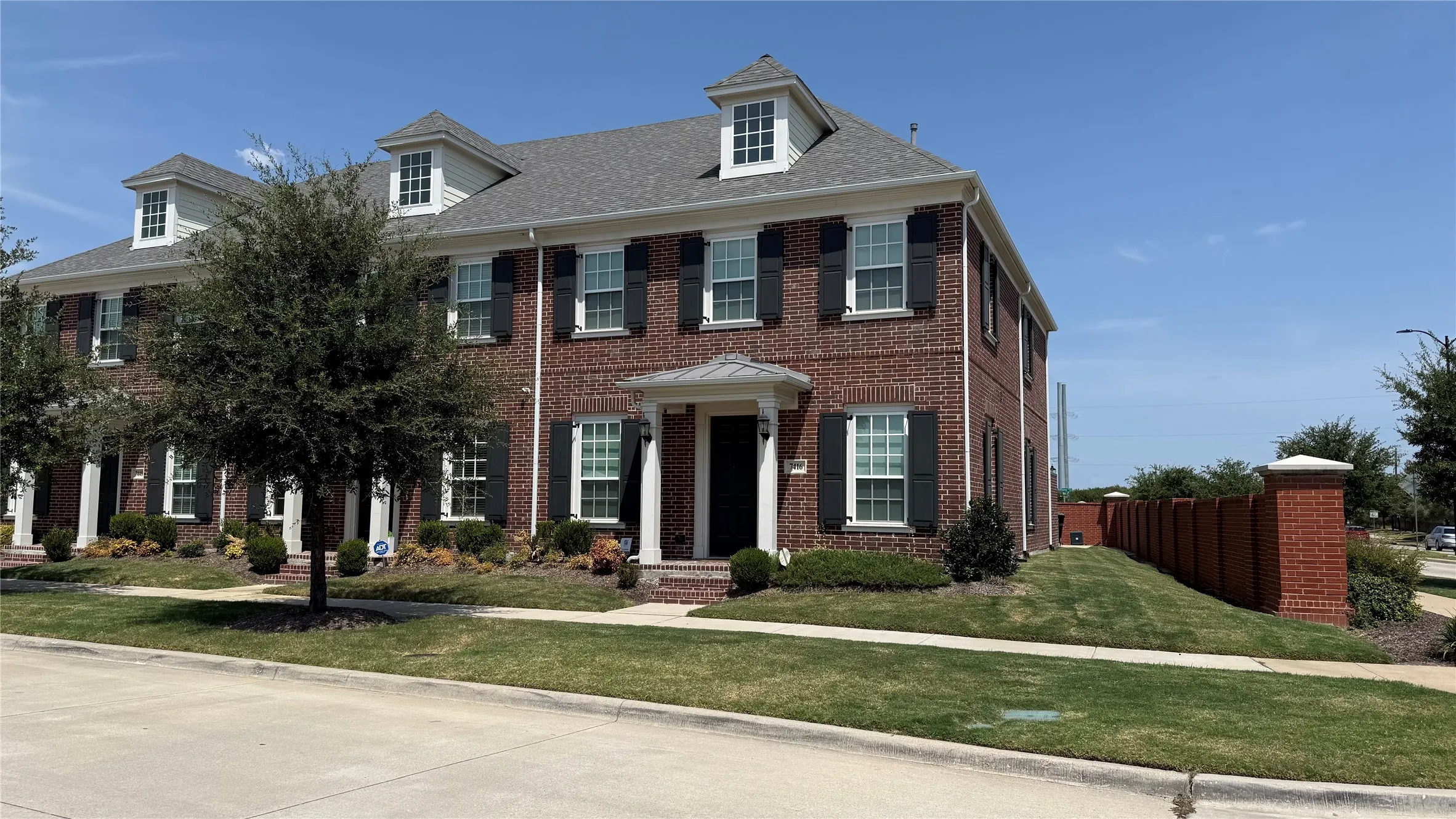 Brick exterior featuring white window frames with dark shutters, multiple dormer windows, and a covered entry