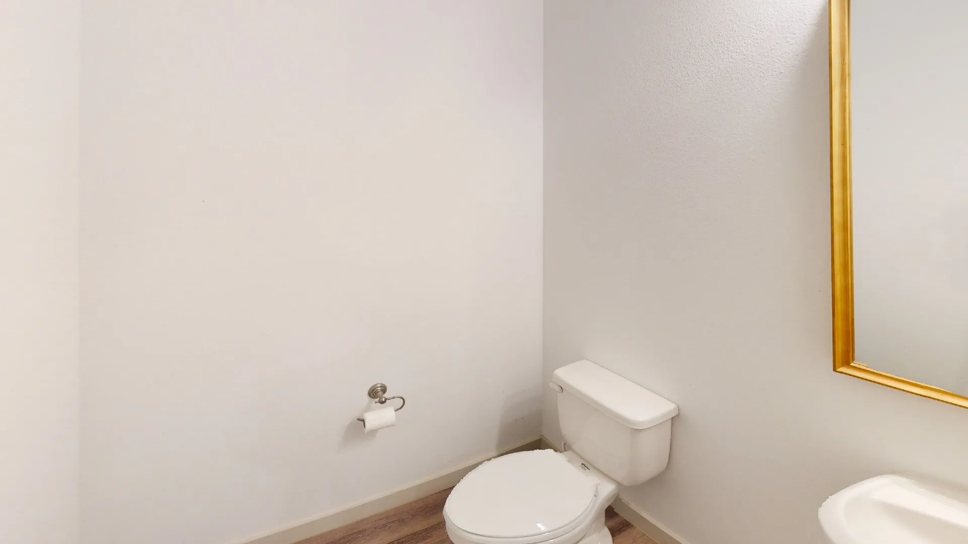 Powder room featuring a white ceramic toilet, wall-mounted chrome fixtures, wood-finish flooring, and soft neutral wall finishes