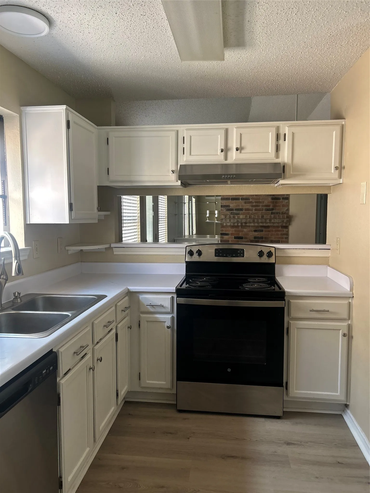 Kitchen featuring white cabinetry, wood-finish flooring, stainless steel sink, and a black range with stainless steel accents