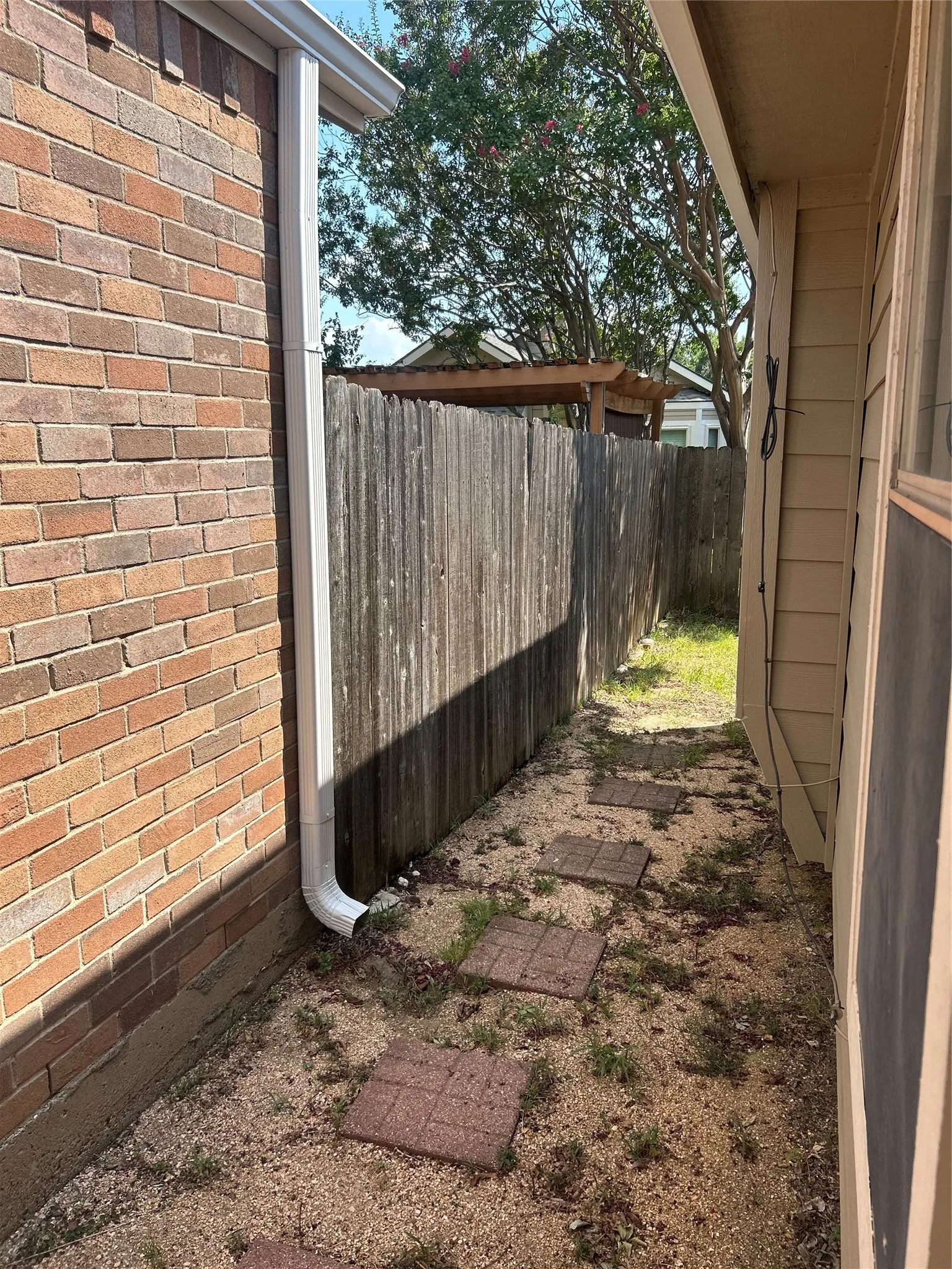 Brick exterior, functional gutter system, wood privacy fence, stepping stone pathway, and gravel ground cover leading to back yard