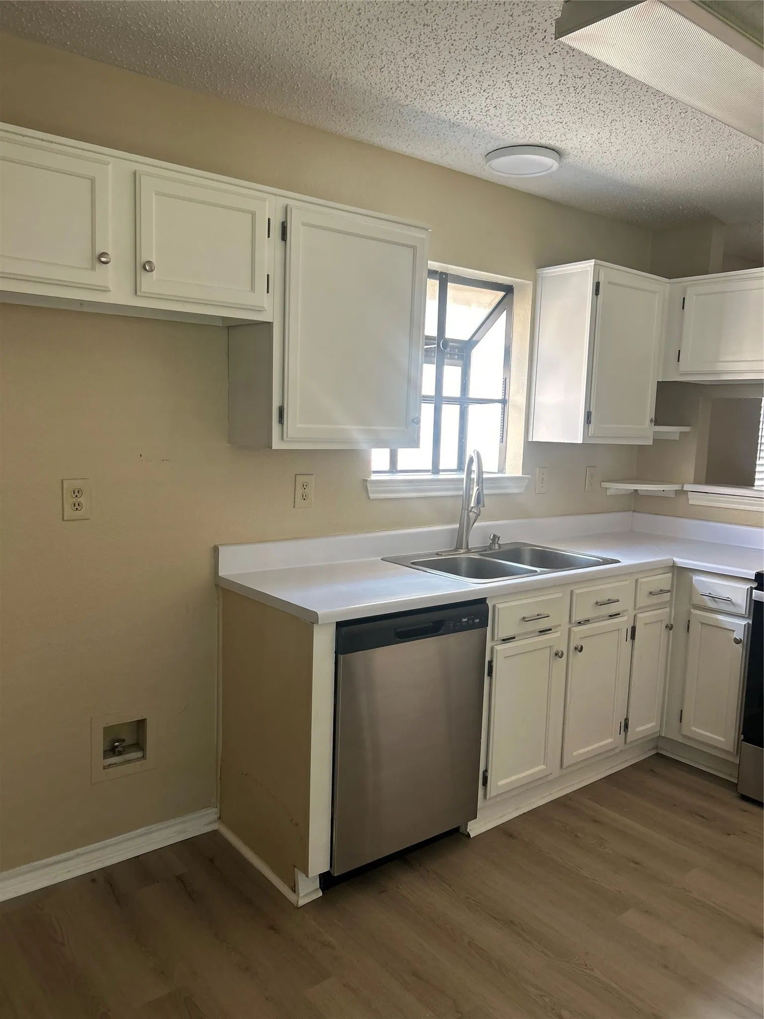 White cabinetry with silver-tone hardware, wood-finish flooring, stainless steel dishwasher, double basin sink with gooseneck faucet, and light countertops