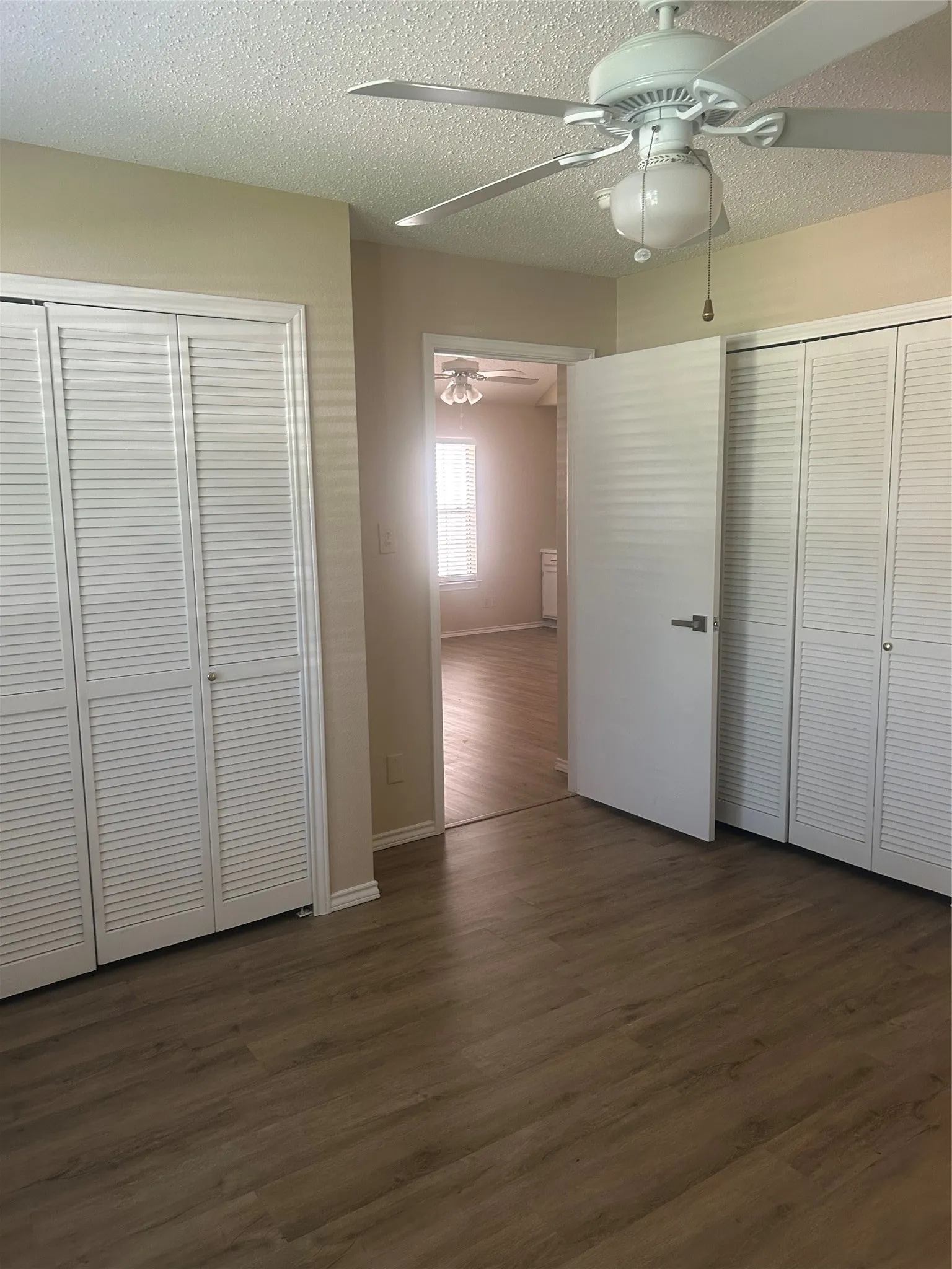 Wood-finish flooring, two sets of louvered bi-fold doors, white interior door, ceiling fan with integrated lighting, and neutral wall paint