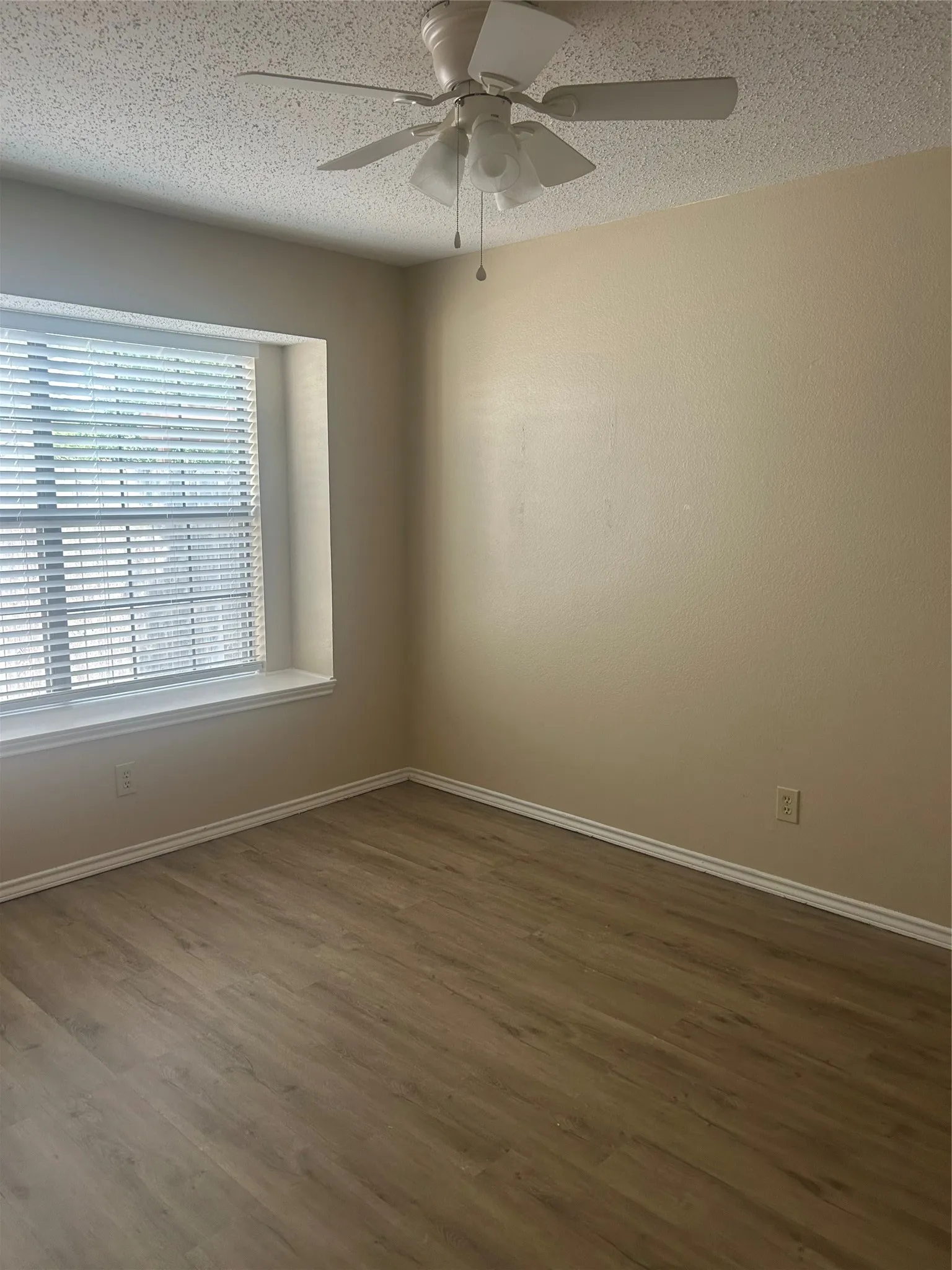 Neutral wall tones with wood-finish flooring, a ceiling fan with integrated lighting, and a window with blinds