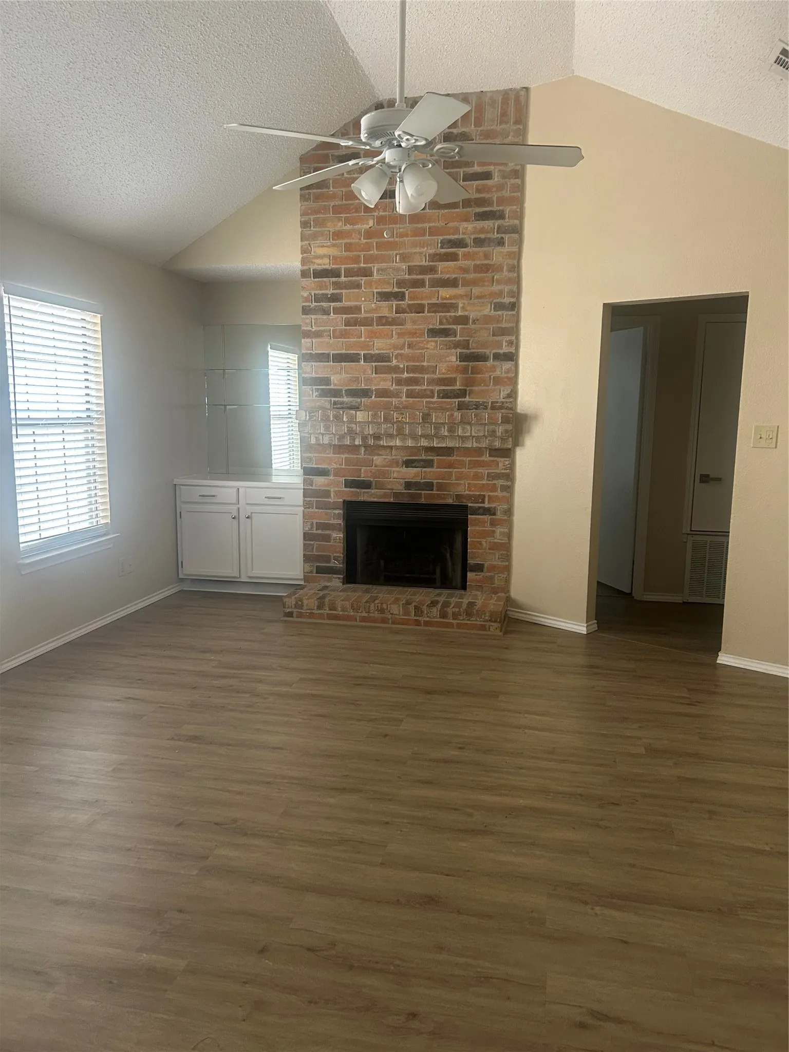Vaulted ceiling with a ceiling fan, brick fireplace, wood-finish flooring, and built-in cabinetry