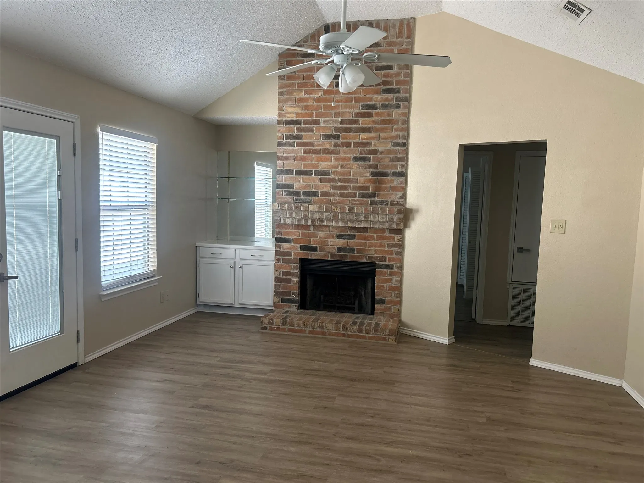 Vaulted ceiling with a ceiling fan, brick fireplace, built-in cabinetry, and wood-finish flooring