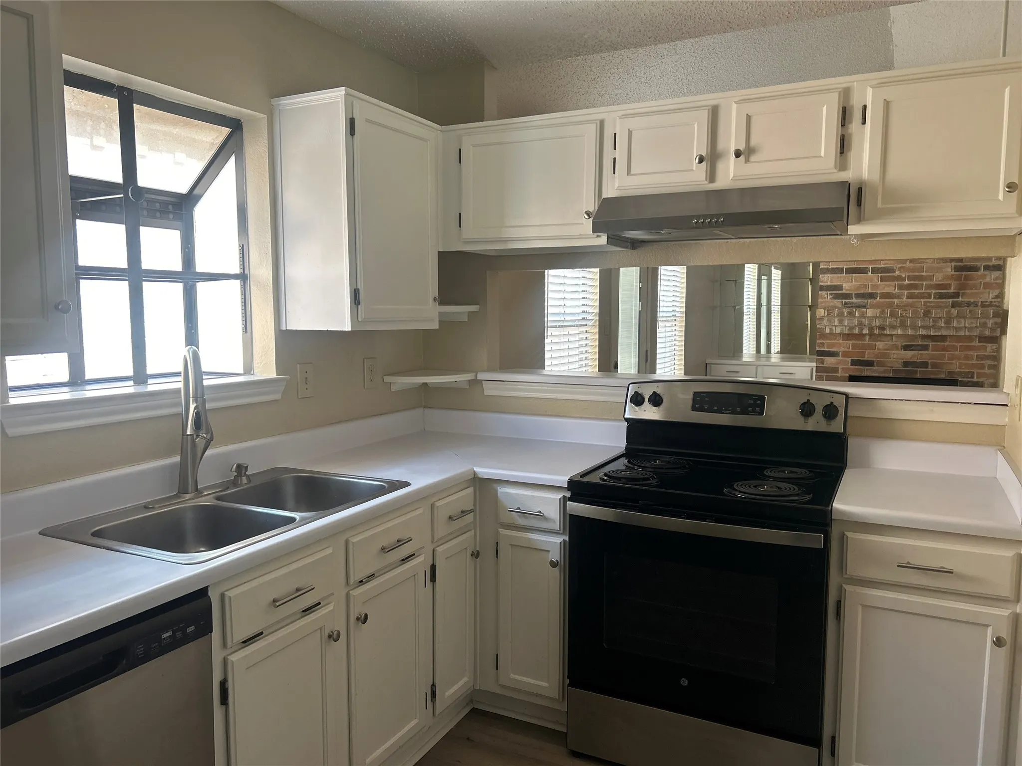 White cabinetry with silver hardware, dual basin stainless steel sink, stainless steel dishwasher, stainless steel electric range, and a built-in range hood