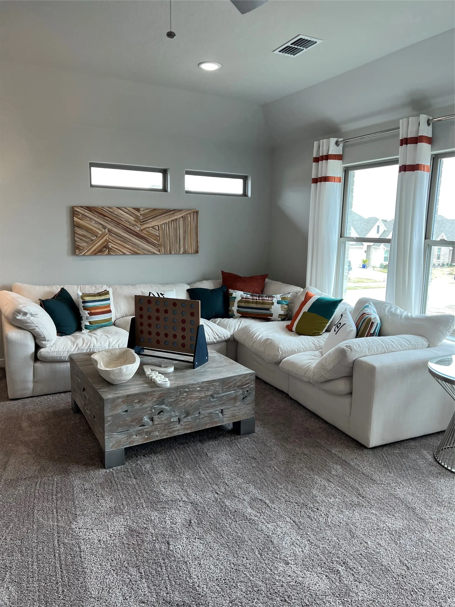 Recessed lighting, high ceilings, rectangular windows, large windows with white sheers, and gray carpet flooring