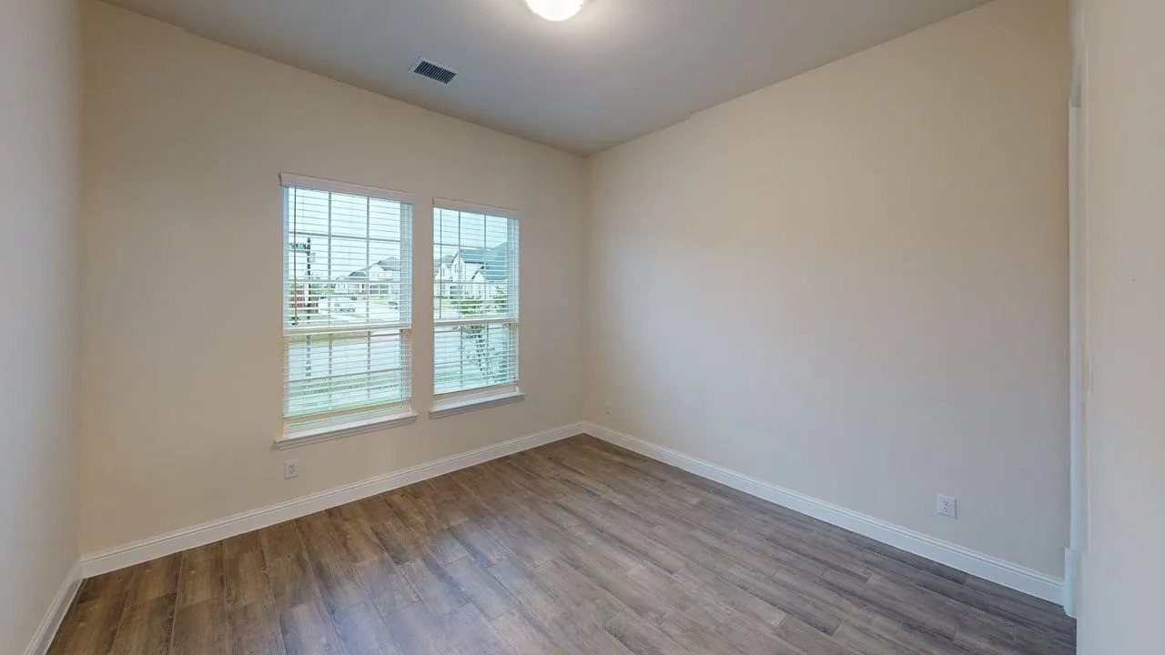 Two large windows with blinds, light-toned walls, wood-finish flooring, and a ceiling-mounted light fixture