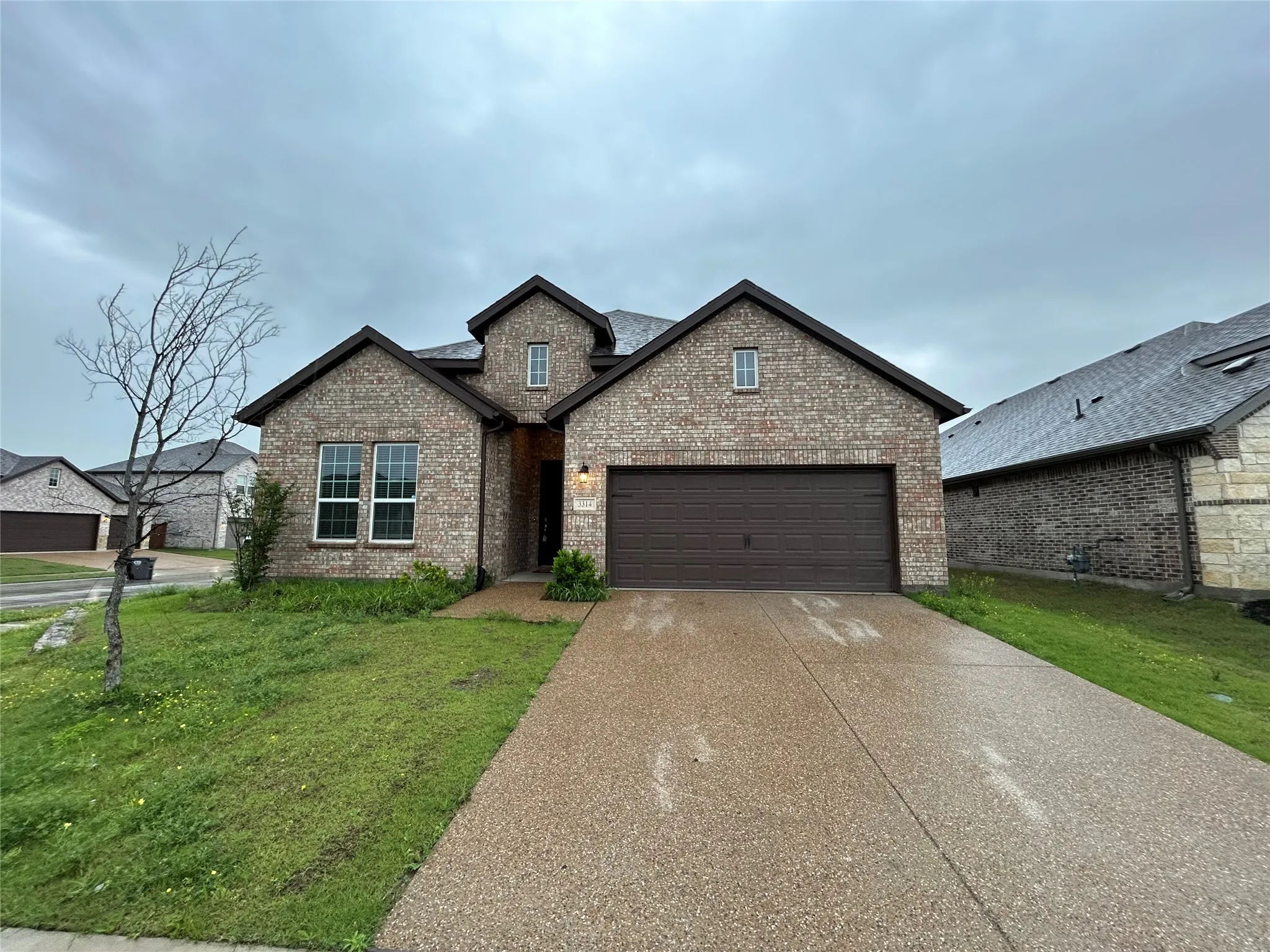 Brick Colonial home featuring a two-car attached garage with dark finish doors, manicured front lawn, and a concrete driveway