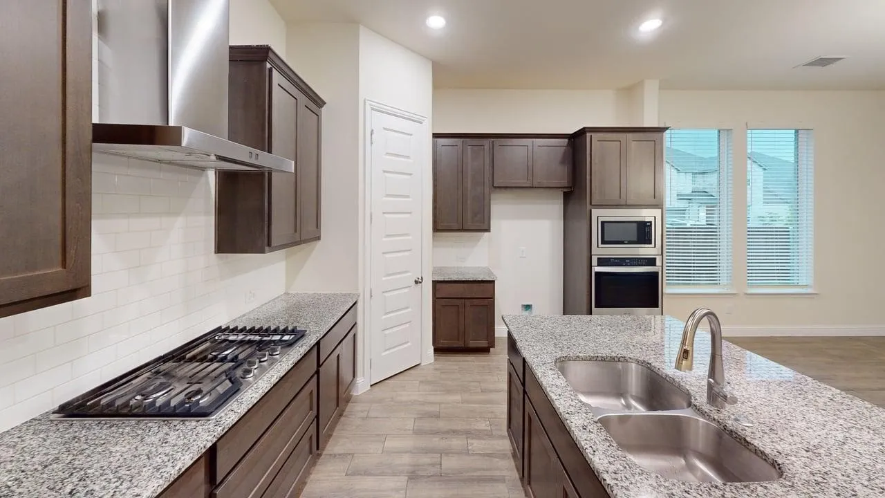Kitchen featuring wood-finish cabinetry, granite countertops, tile backsplash, built-in stainless steel appliances, and a kitchen island with an undermount double sink