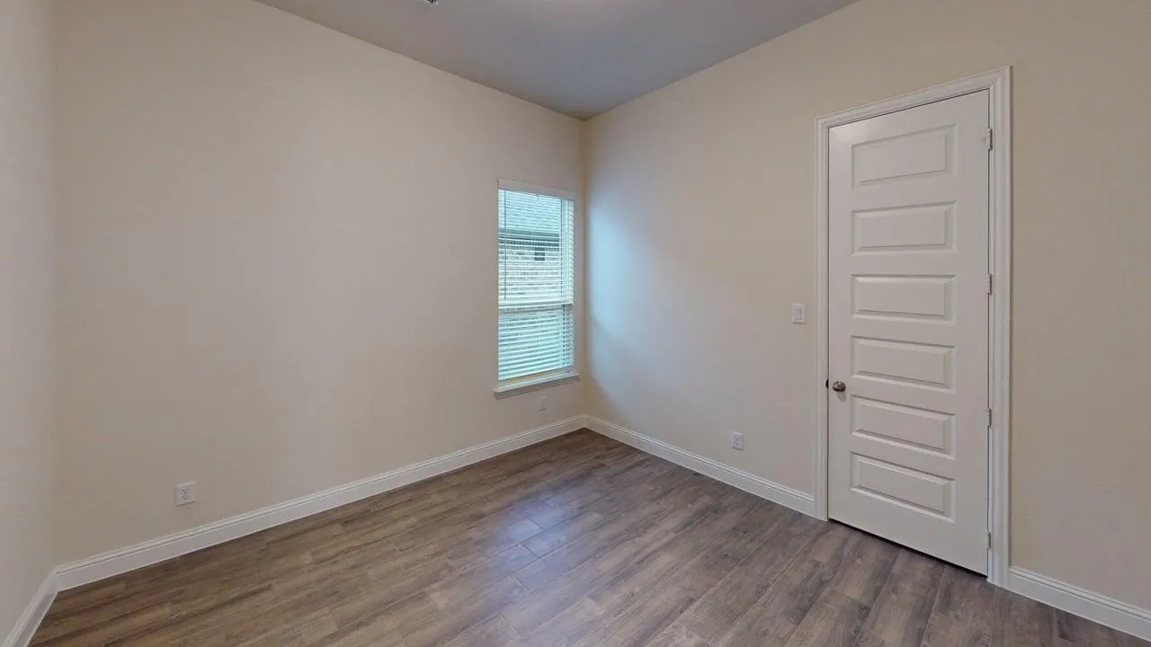 Bright corner bedroom with wood-finish flooring, large window with natural light, and smooth five-panel closet door