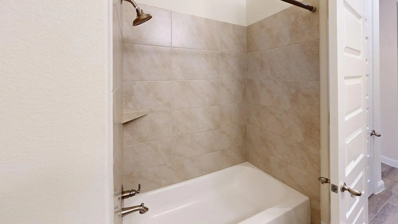 Updated primary bathroom featuring a tile-lined shower enclosure with brushed nickel fixtures, a white soaking tub with integrated surround, and neutral stone-finish wall treatments throughout