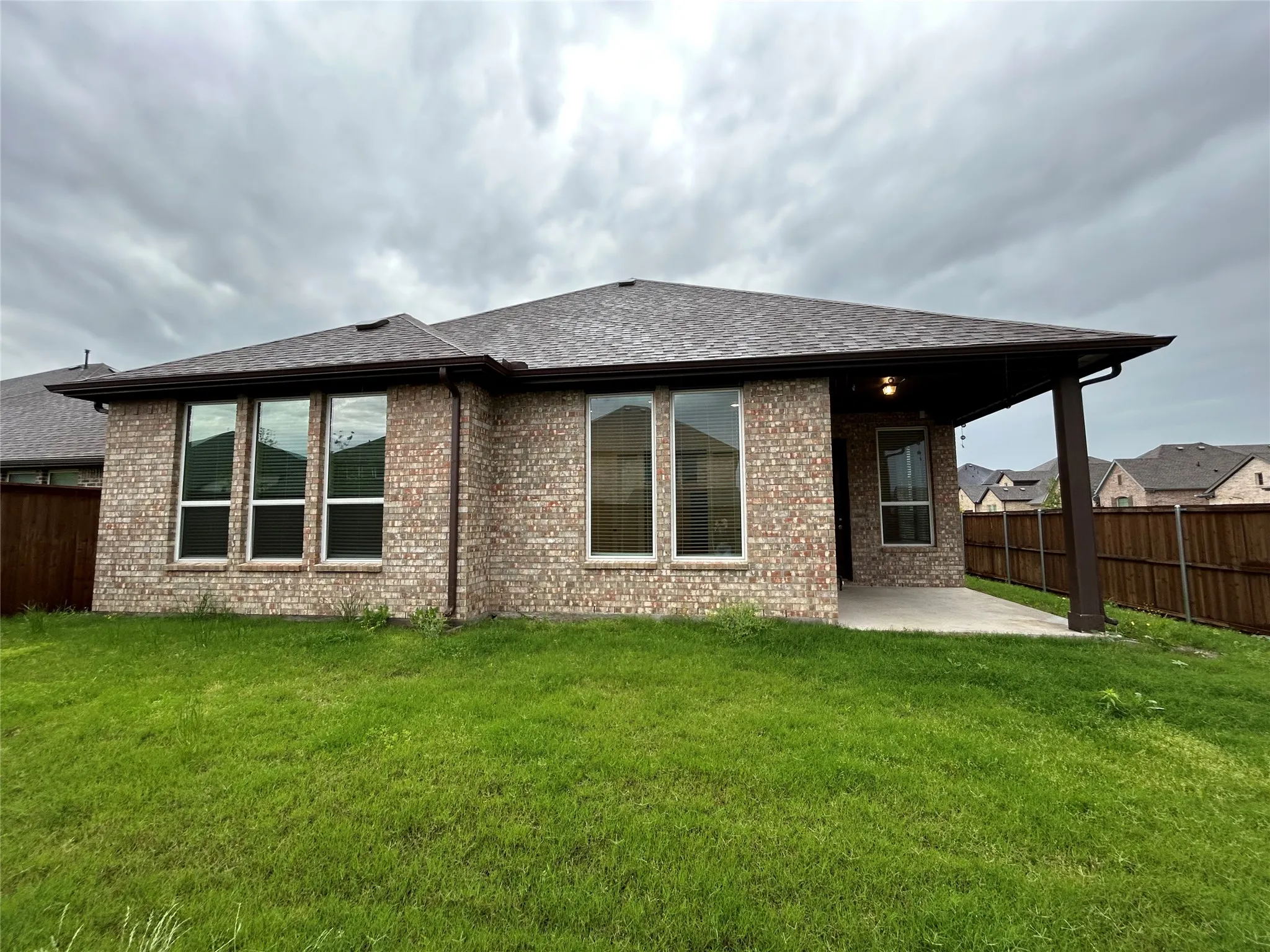 Brick exterior with multiple windows, a covered patio, and a shingled roof