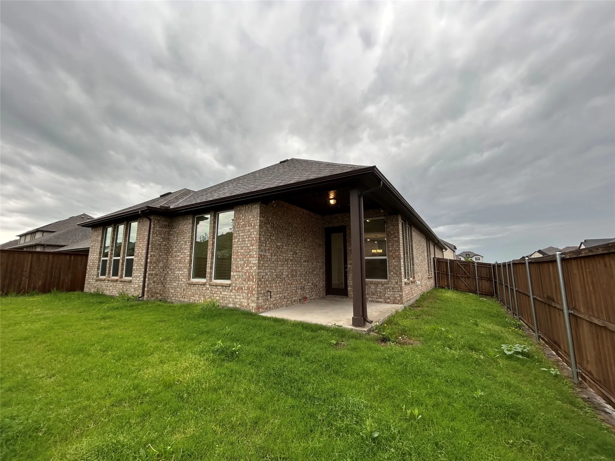 Modern brick residence with expansive covered patio, large multi-pane windows, and manicured lawn with mature landscaping and privacy fencing