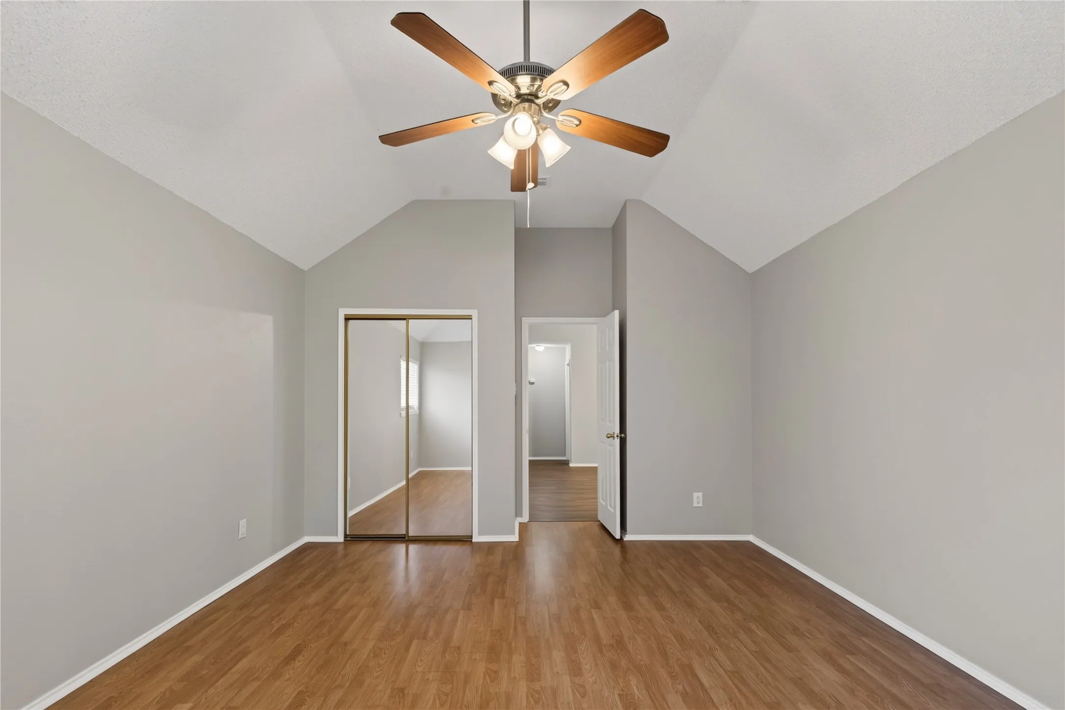 Vaulted ceilings, wood-finish flooring, ceiling fan with integrated lighting, and mirrored closet doors