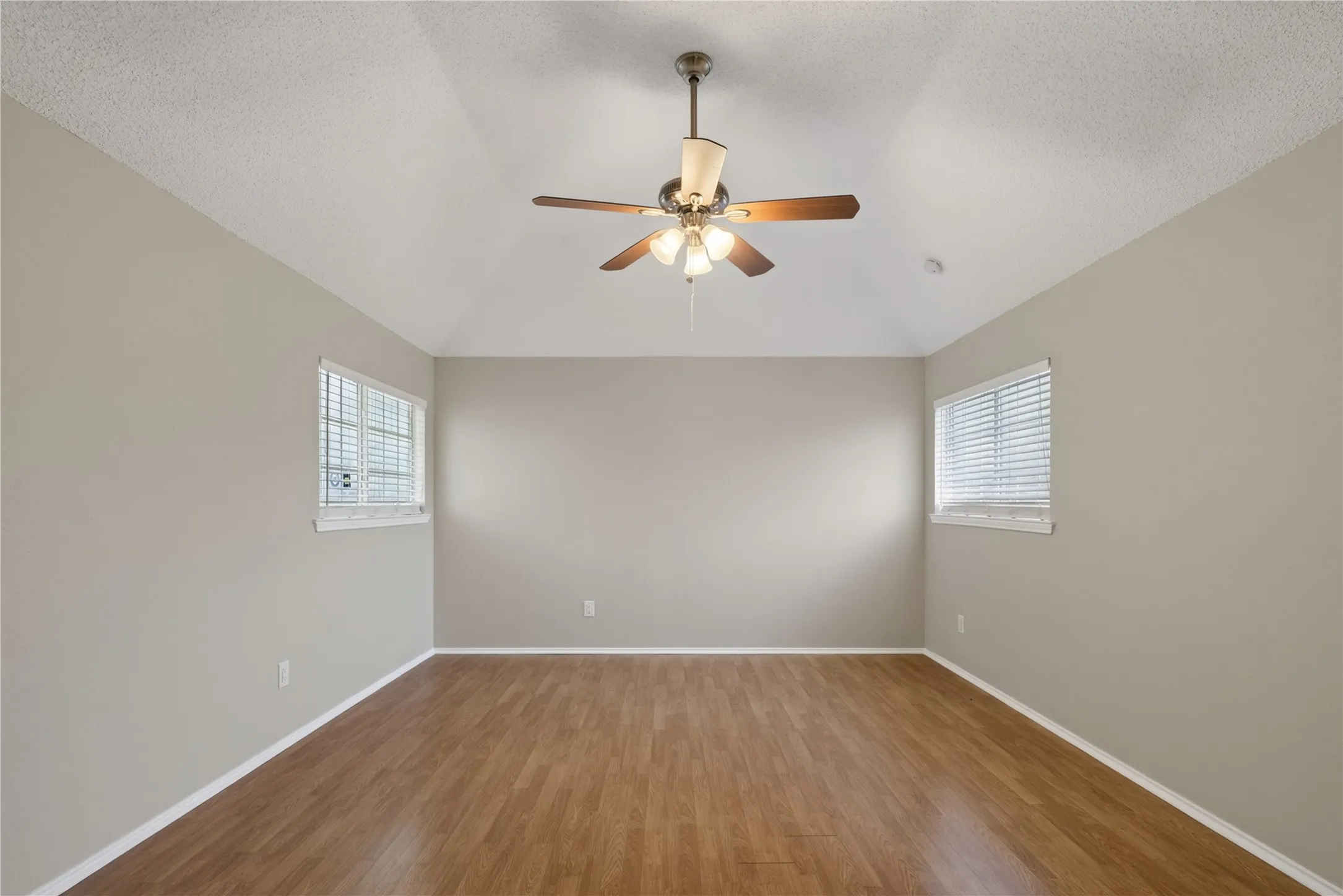 Vaulted ceiling with a ceiling fan, wood-finish flooring, and two windows with blinds
