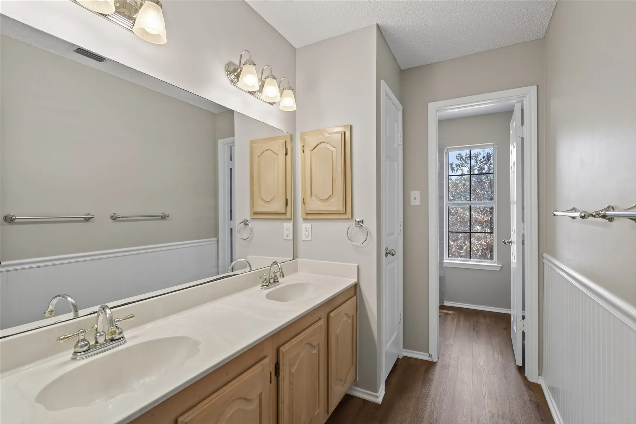 Dual vanity with integrated sinks, wood-finish cabinetry, and overhead bar lighting