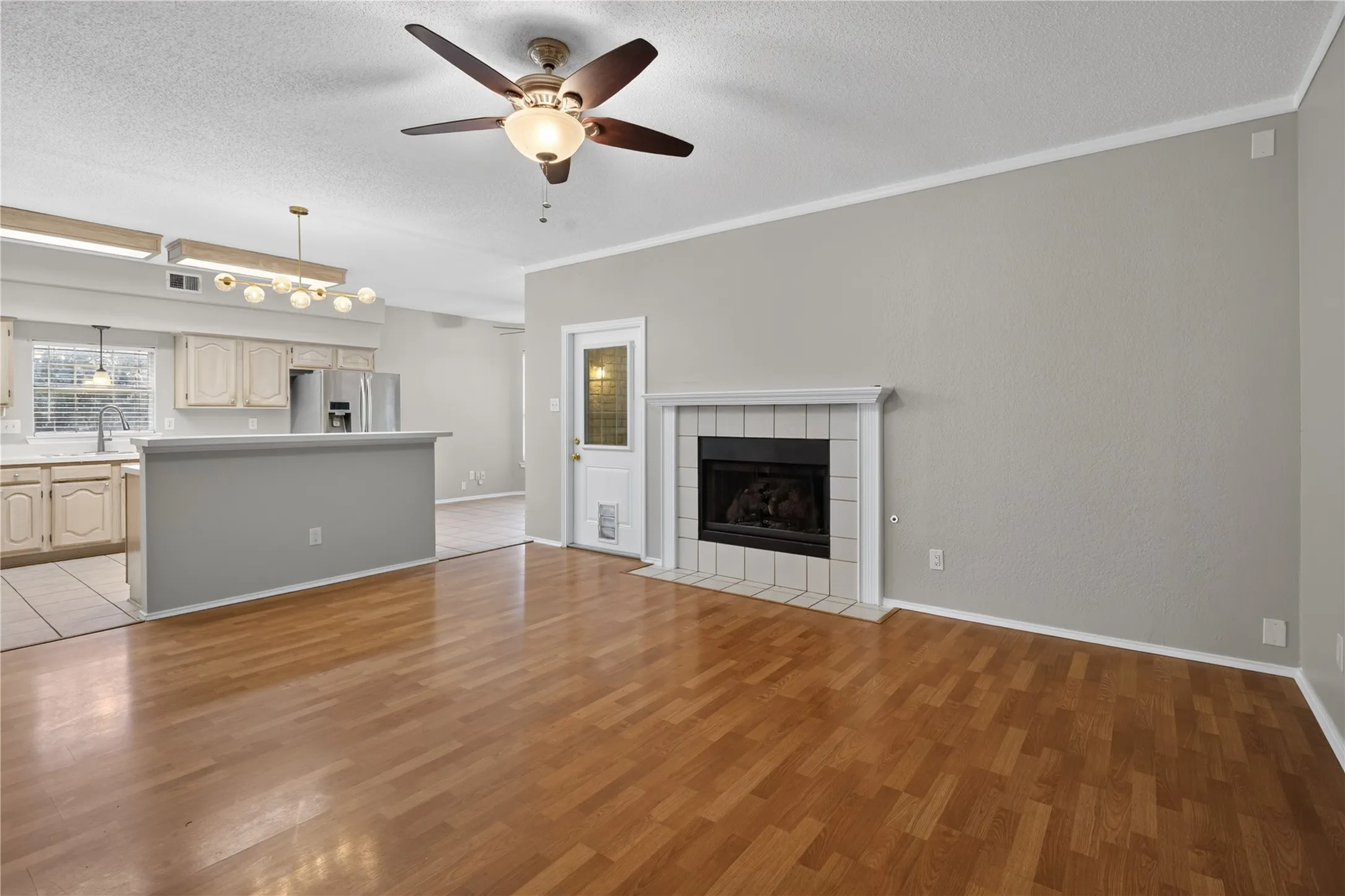 Hardwood flooring, ceiling fan, fireplace with tile surround, kitchen with light cabinetry, and a peninsula counter