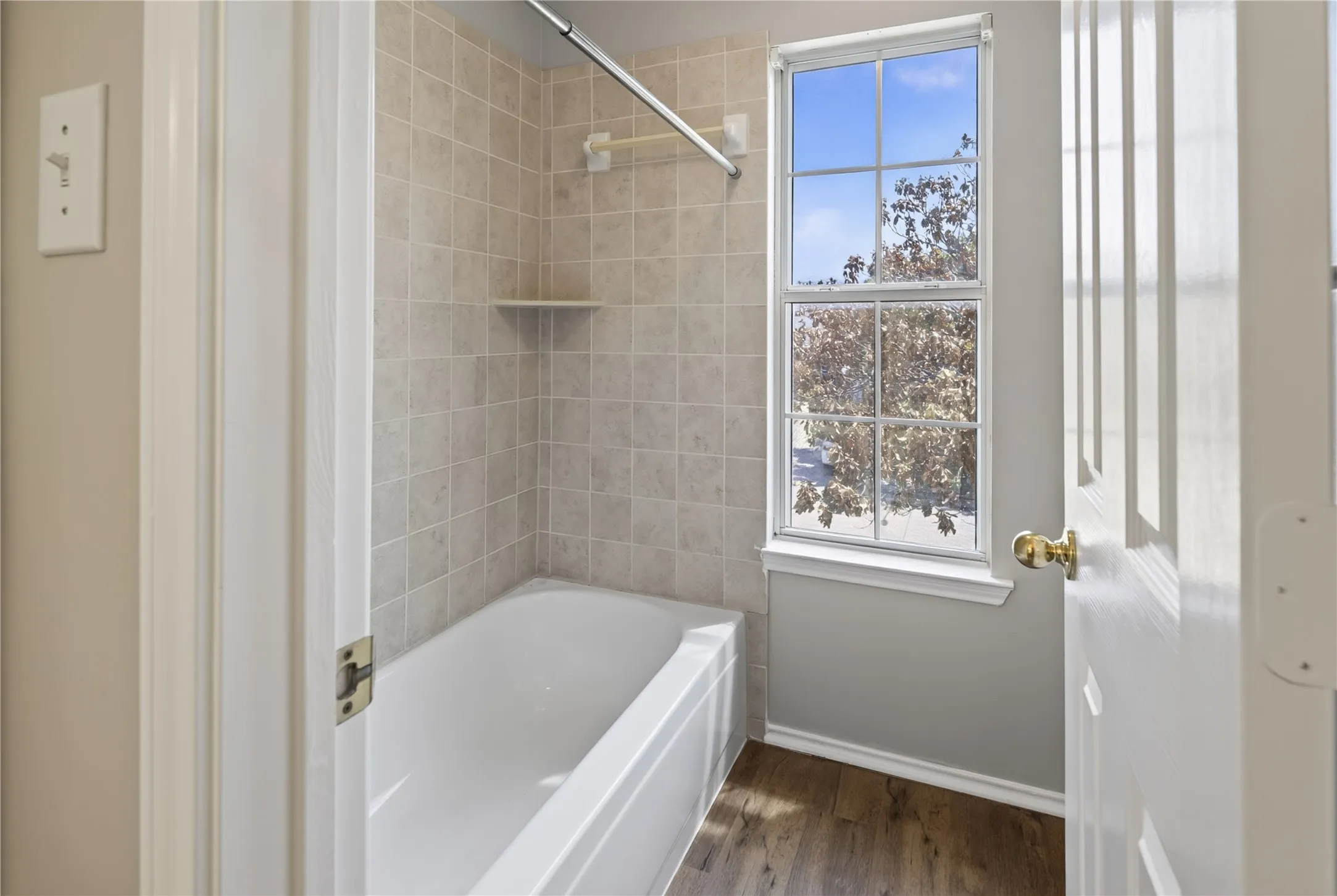 Bathtub with light-toned tiled surround, integrated shower shelf, and a large window