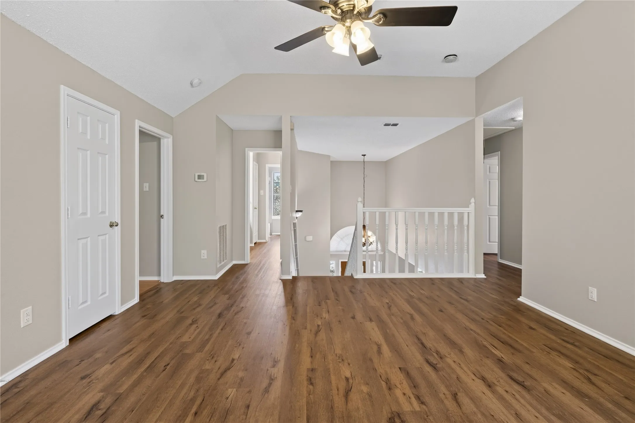 Vaulted ceiling with a ceiling fan, wood-finish flooring, white paneled interior doors, and white railing