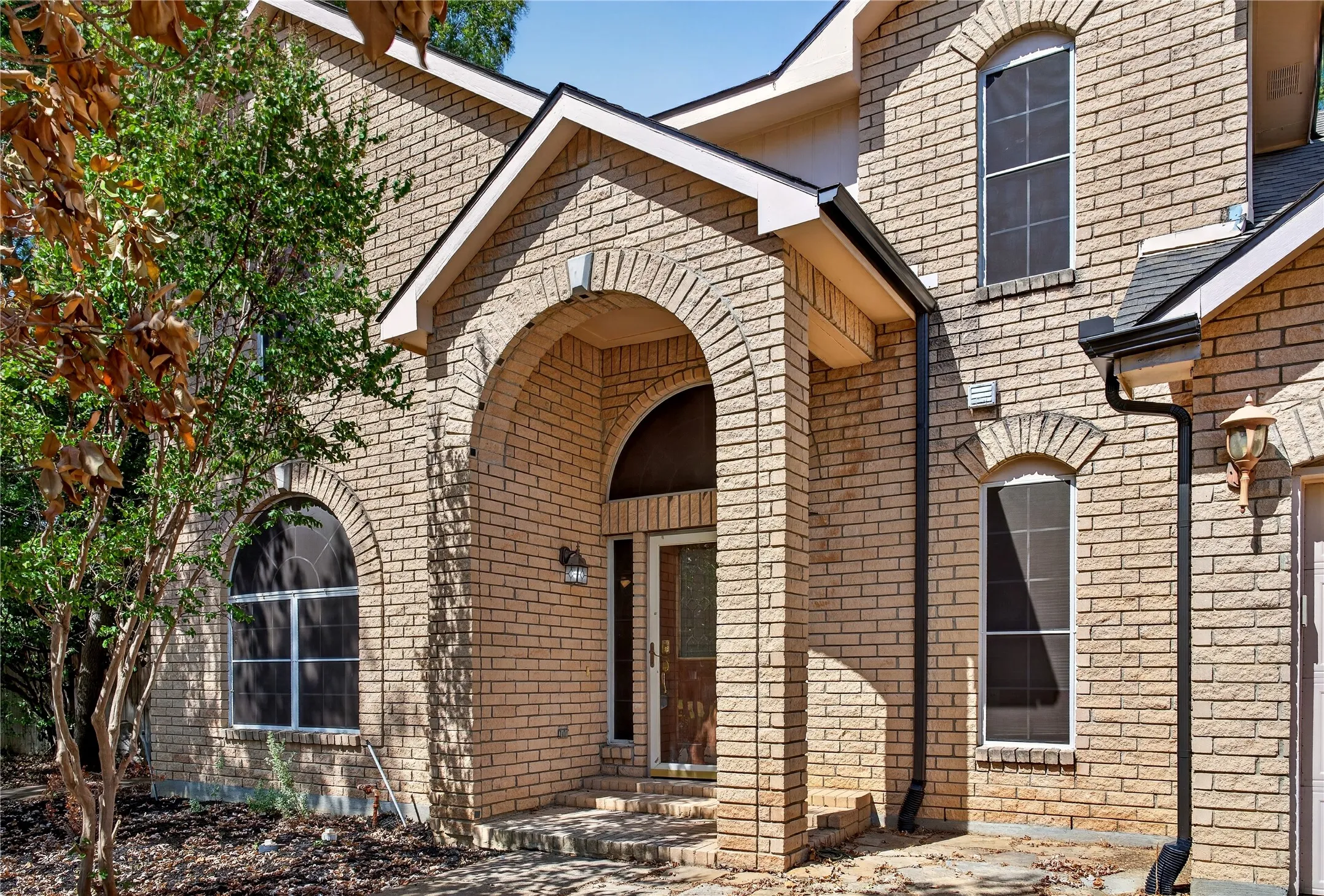 Brick exterior featuring an arched entry, multiple arched windows, and a black shingle roof