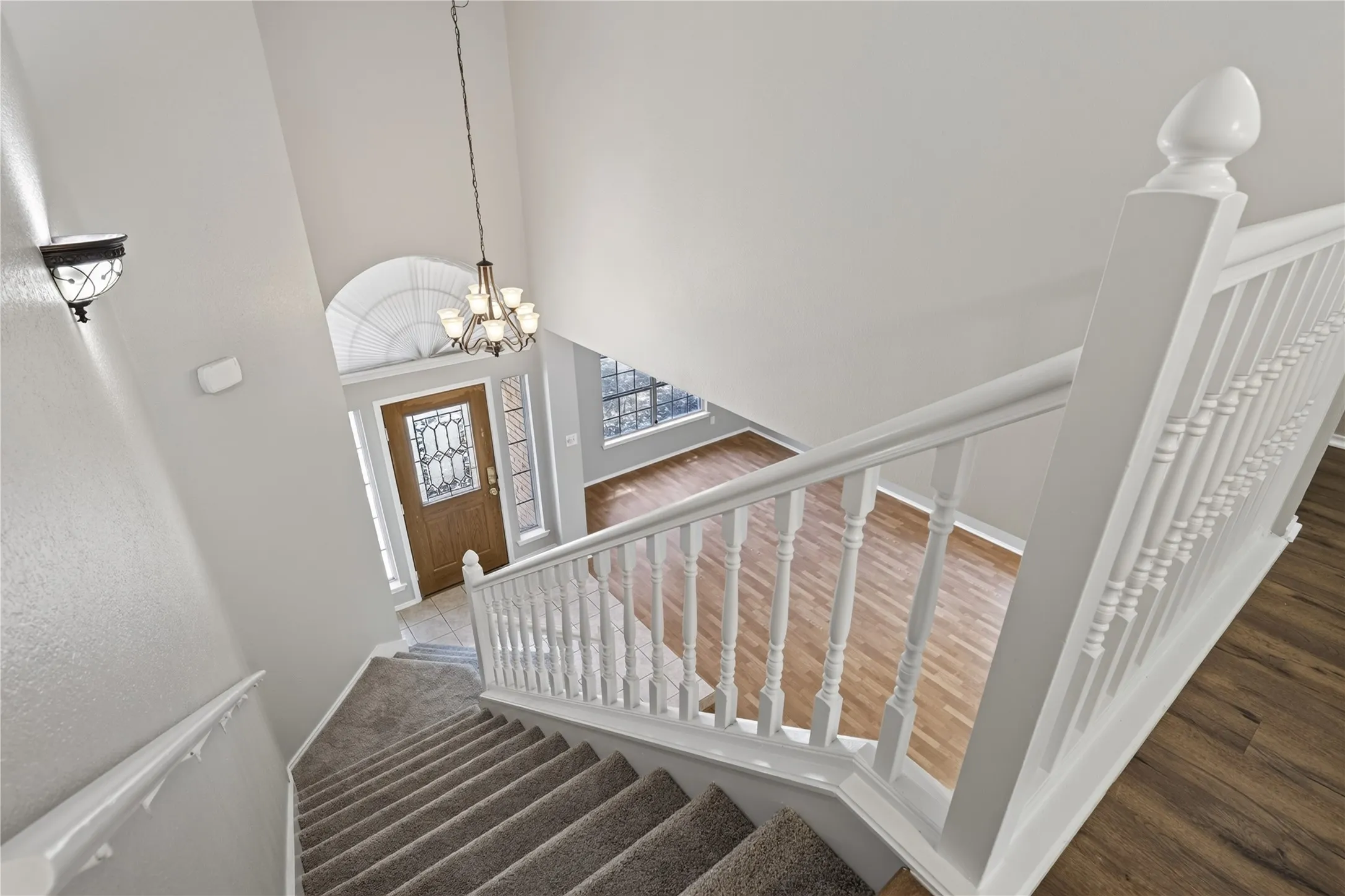 Two-story entryway with a decorative front door, arched transom window, and a multi-arm chandelier