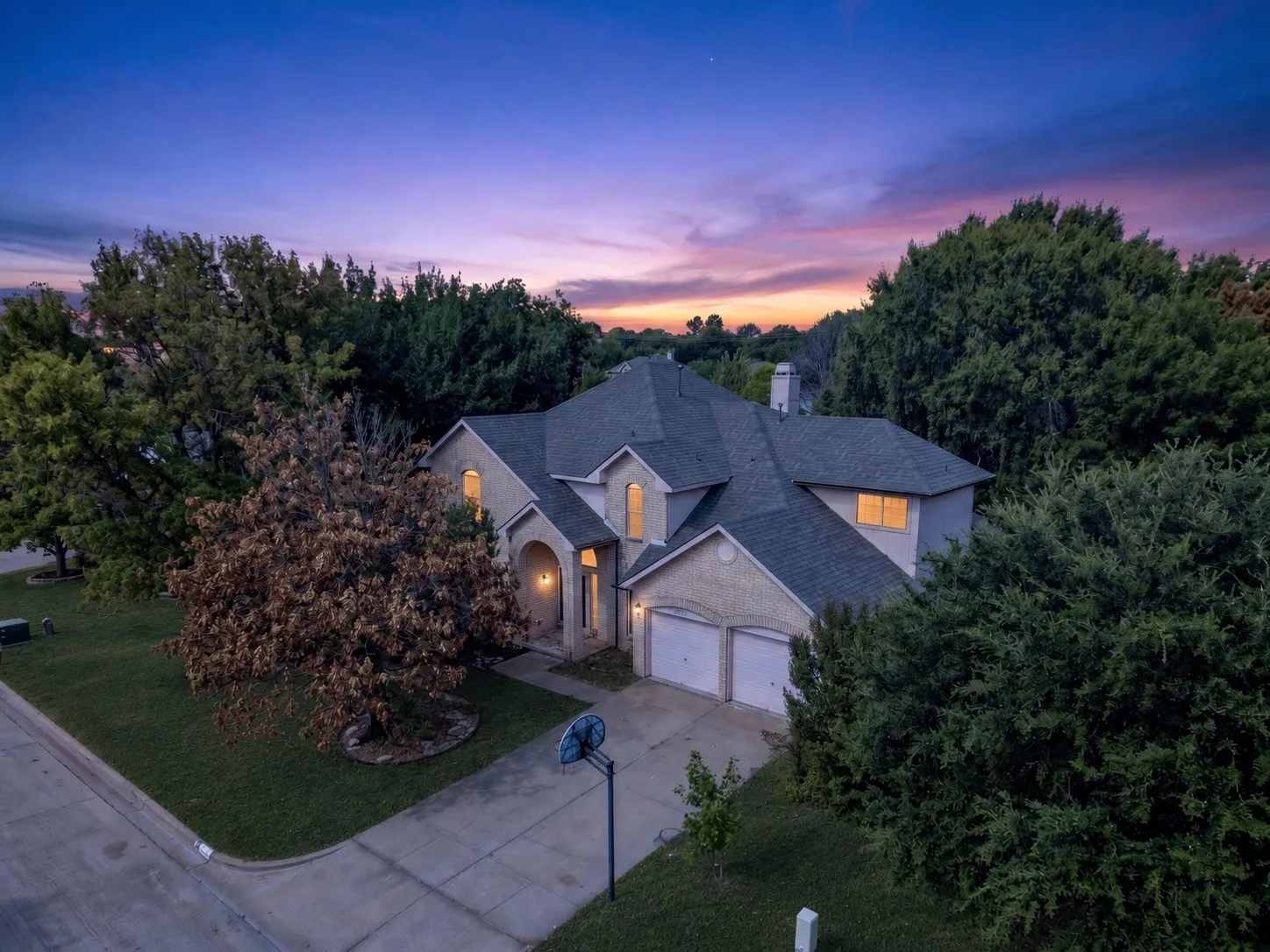 Stucco exterior with brick accents, arched entry, dual garage doors, and mature landscaping - virtually added green grass