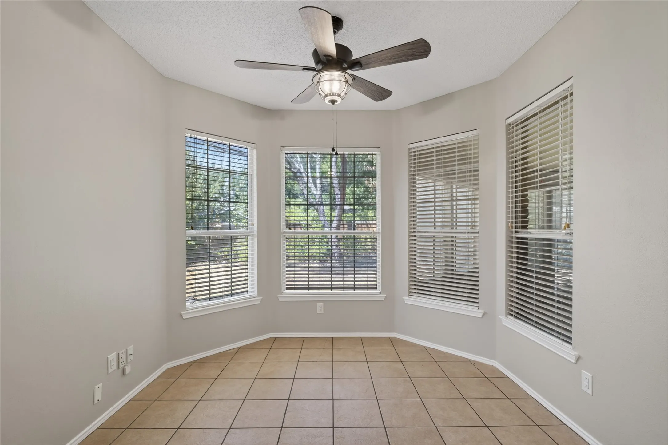 Bay window with three large windows, a ceiling fan with integrated lighting, and tile flooring