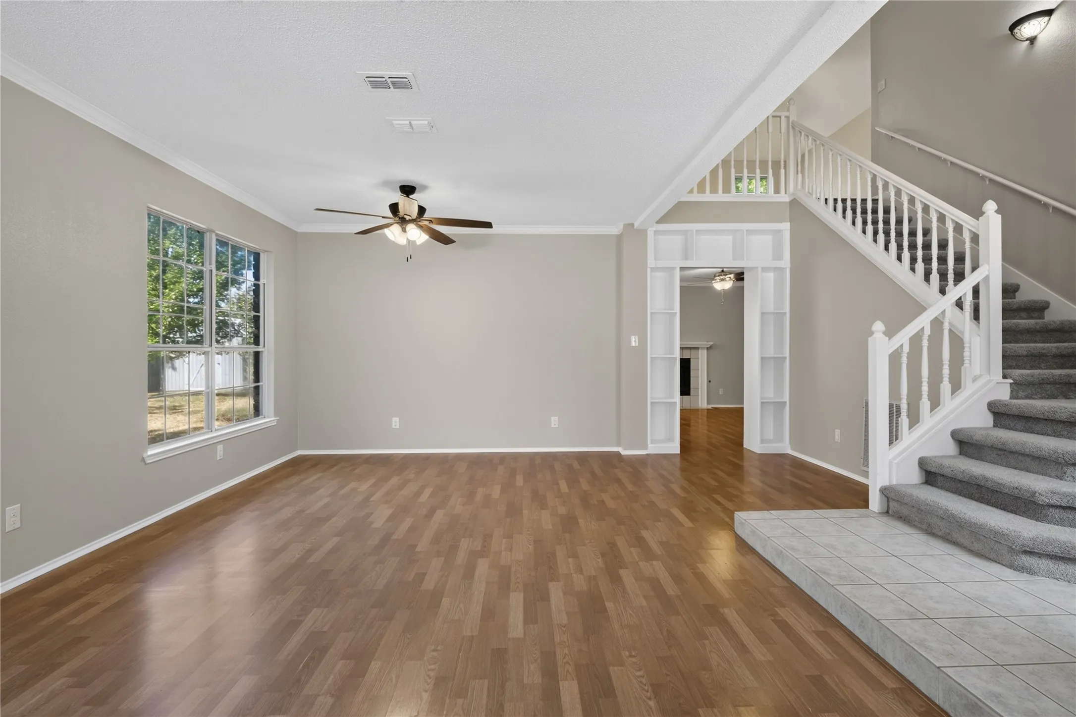 Wood-finish flooring, ceiling fan with integrated lighting, white trim and crown molding, and a carpeted staircase with white railings