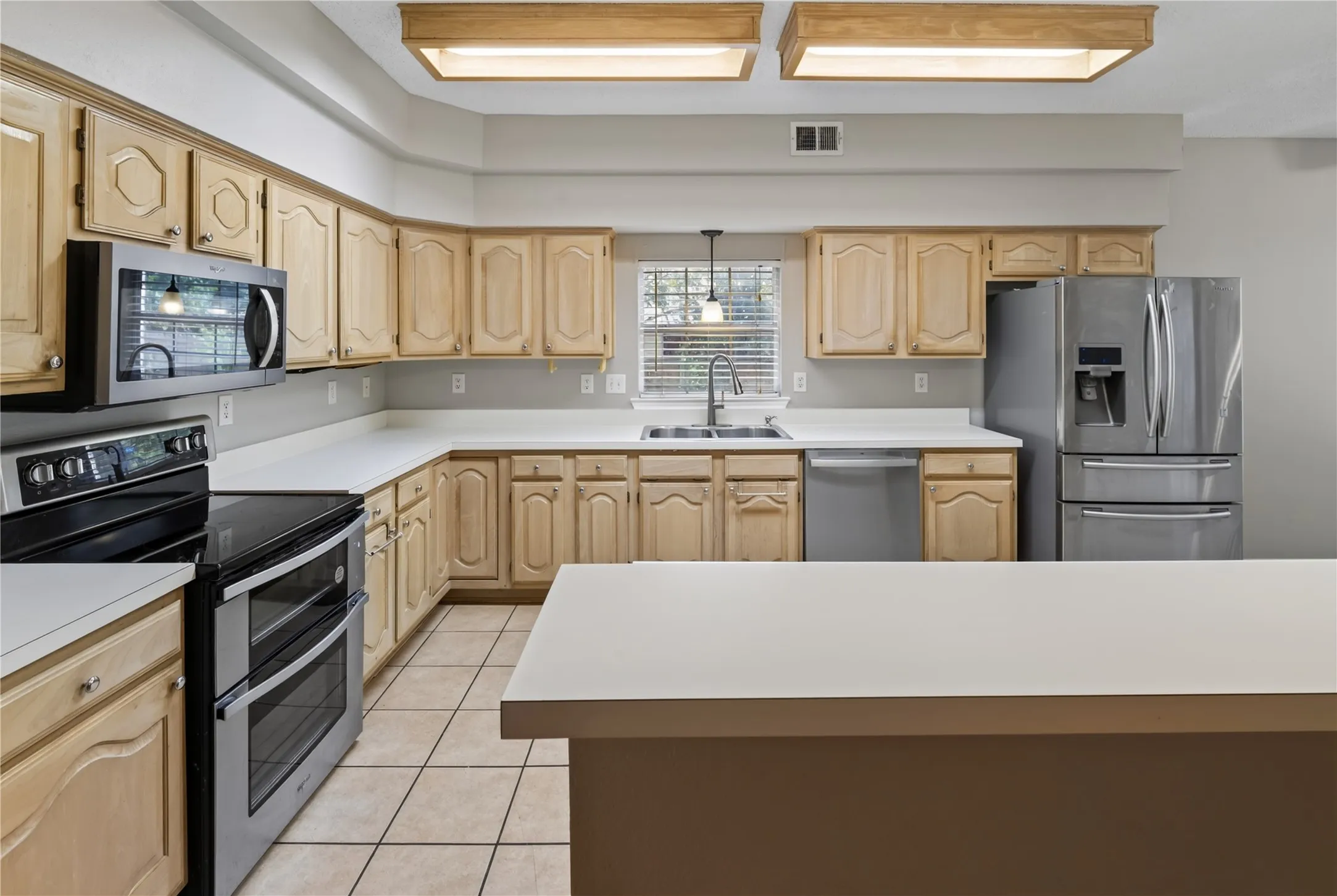 Kitchen with light wood-finish cabinetry, white countertops, and stainless steel appliances