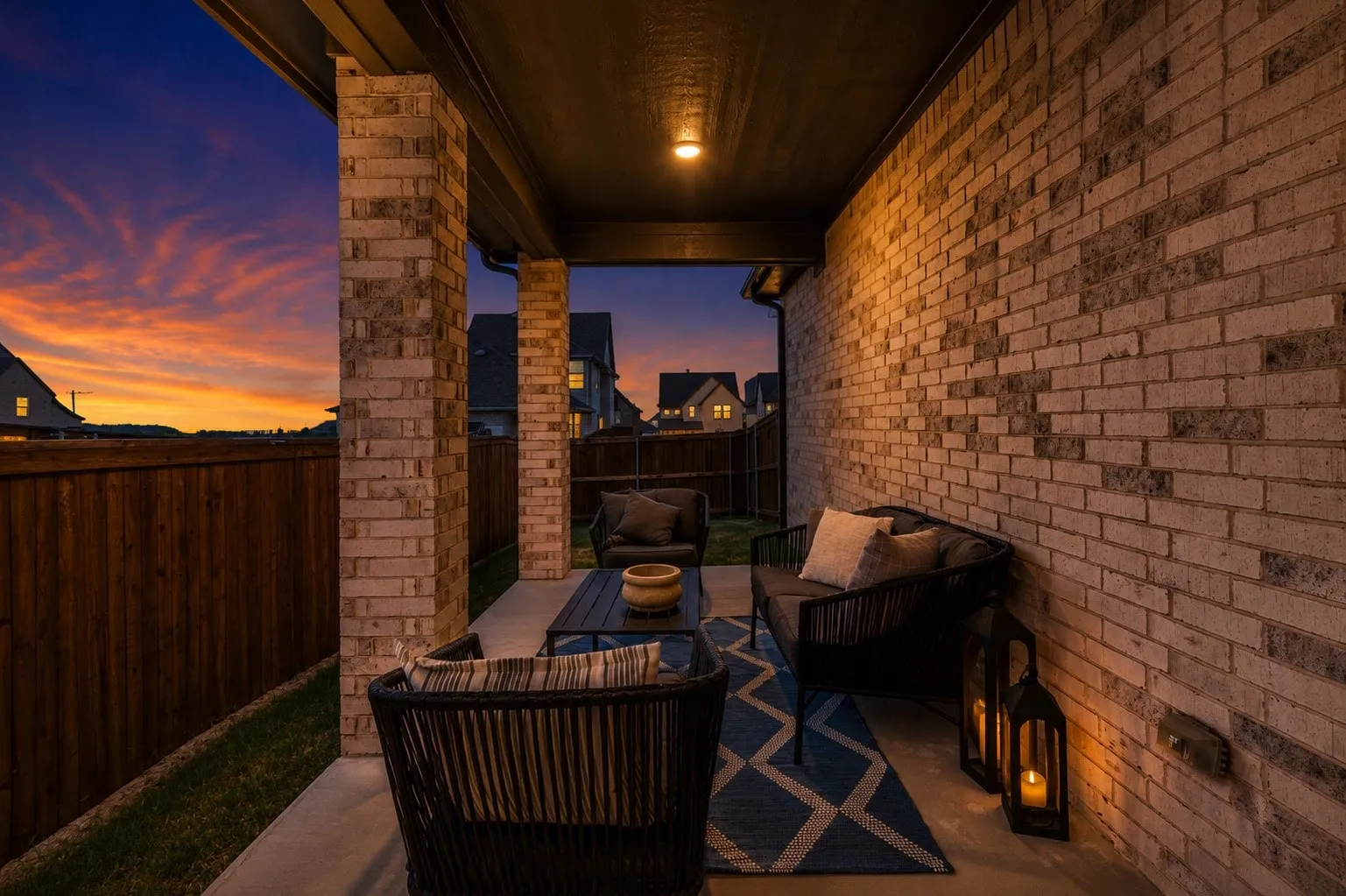 Covered patio with brick construction and ambient overhead lighting, furnished with weather-resistant seating and anchored by a geometric area rug