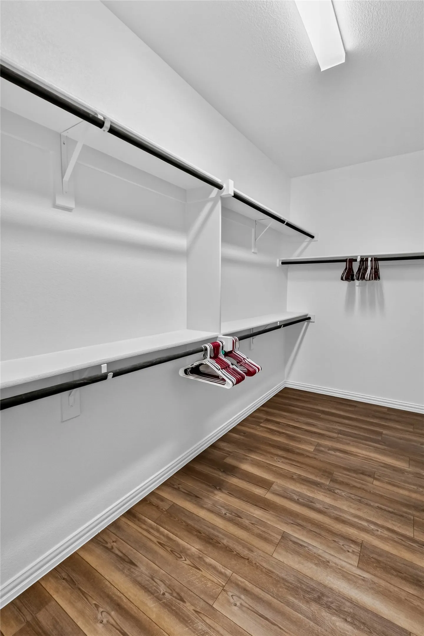 Walk-in closet featuring wood-finish flooring, white shelving, and dual-level hanging rods