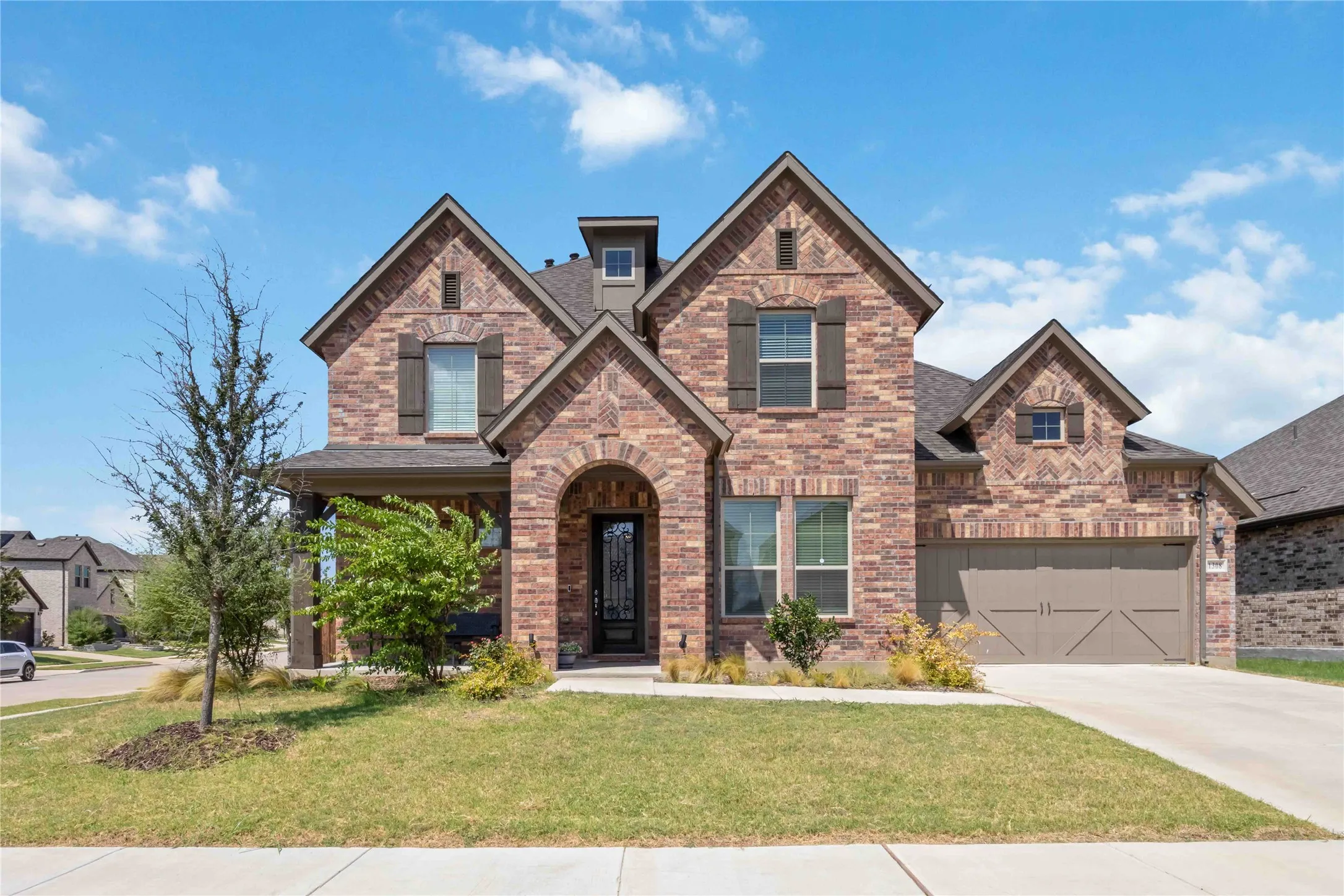 Brick exterior with stone accents, arched entry, two-car garage, and shuttered windows