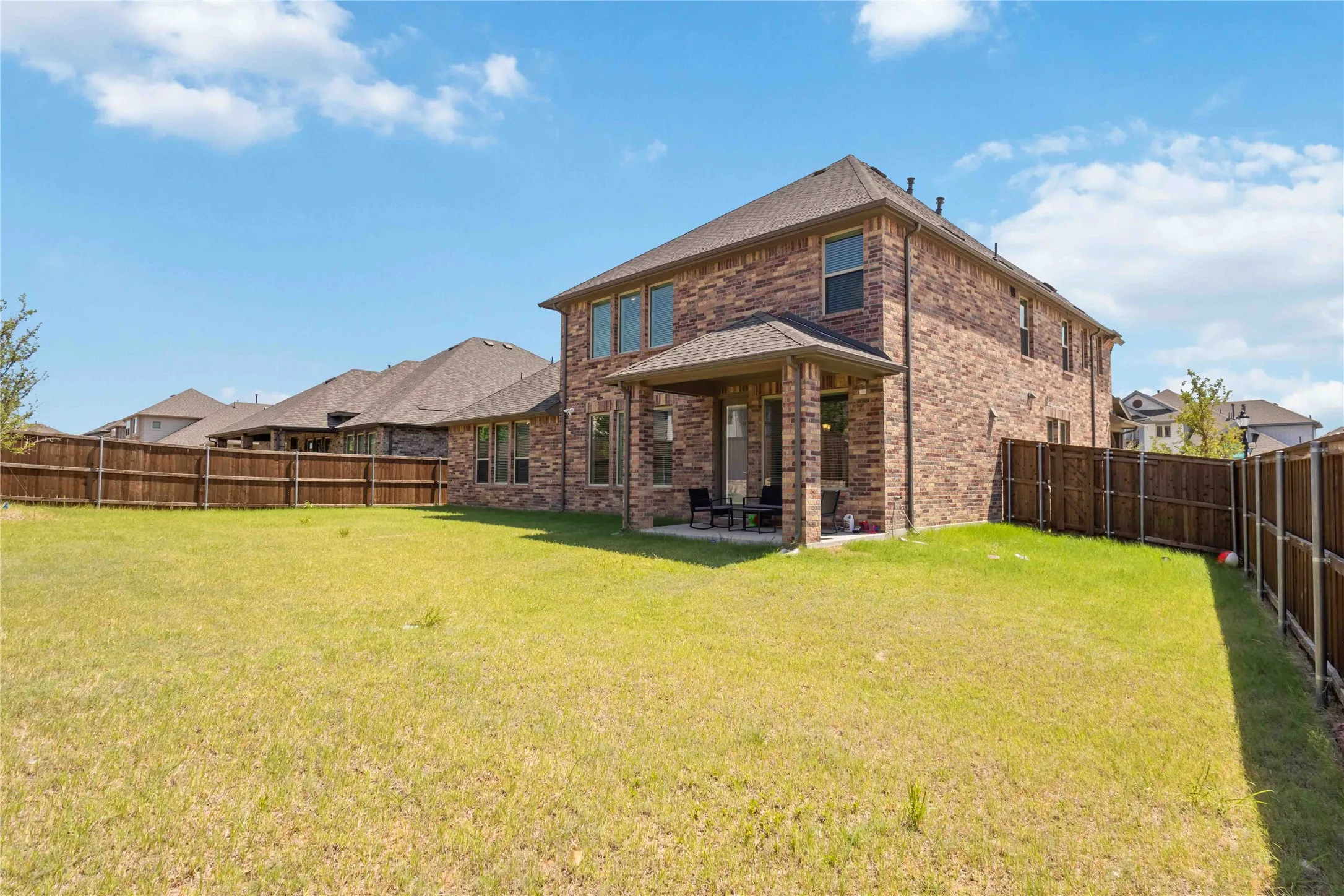 Brick two-story home with expansive rear yard featuring mature landscaping, wooden privacy fencing, and manicured lawn