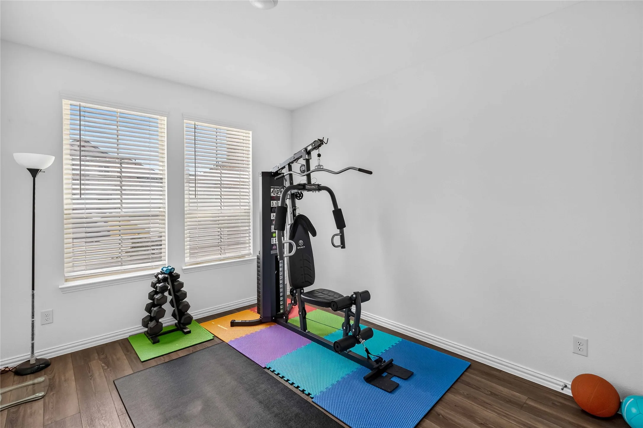 Dedicated home fitness studio featuring polished wood-finish flooring, expansive windows with plantation shutters providing natural light, and ample space for exercise equipment and free weights