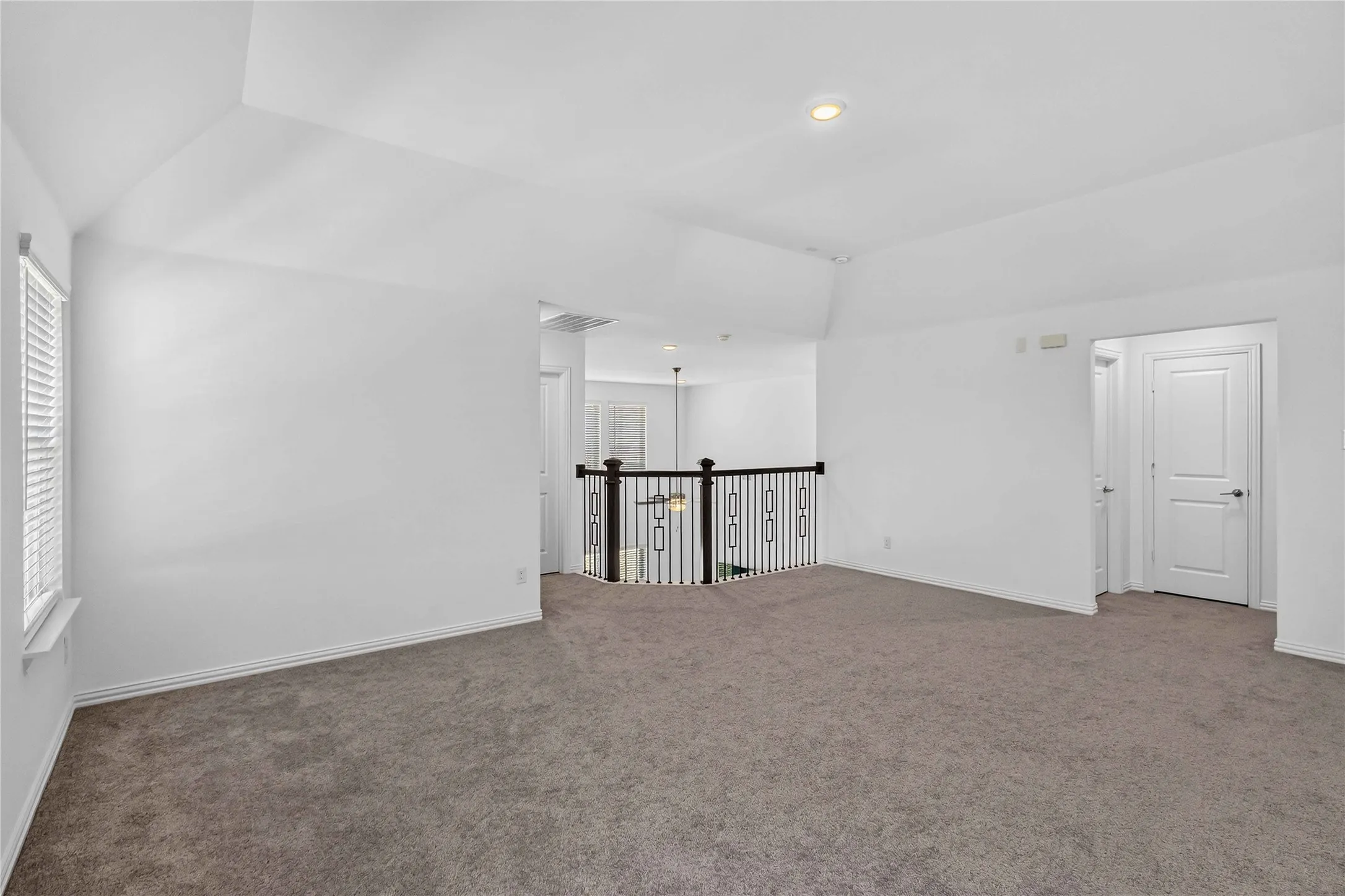 Spacious loft-style room featuring soaring ceilings with recessed lighting, plush carpeting throughout, and a black metal safety railing