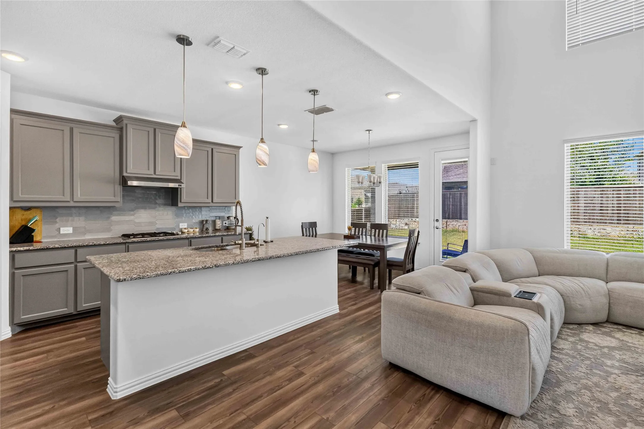 Open-concept living space featuring a chef's kitchen with gray cabinetry, granite countertops, stainless steel appliances, and a large white island with seating, paired with a comfortable lounge area