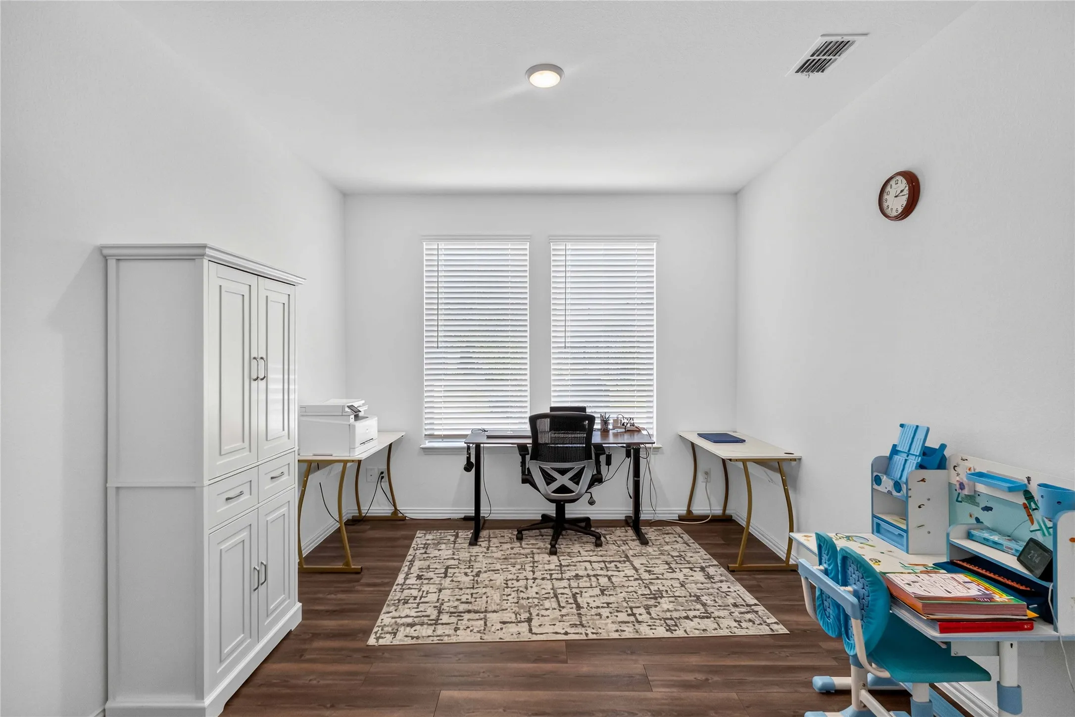 Bright, naturally lit home office featuring white shaker-style cabinetry, wood-finish flooring, plantation shutters, and recessed ceiling lighting