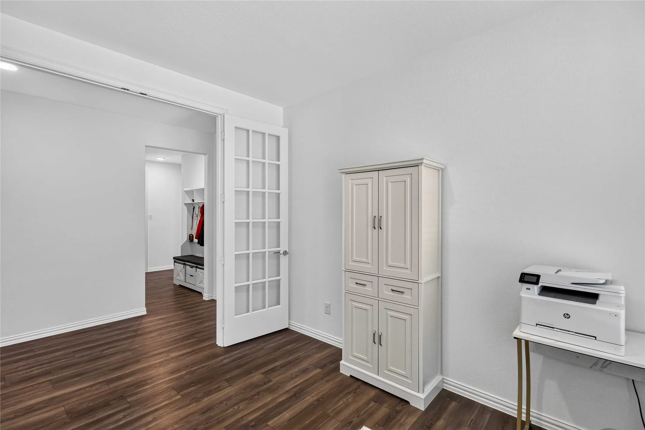 Wood-finish flooring, white walls, and a white built-in storage cabinet with panel doors