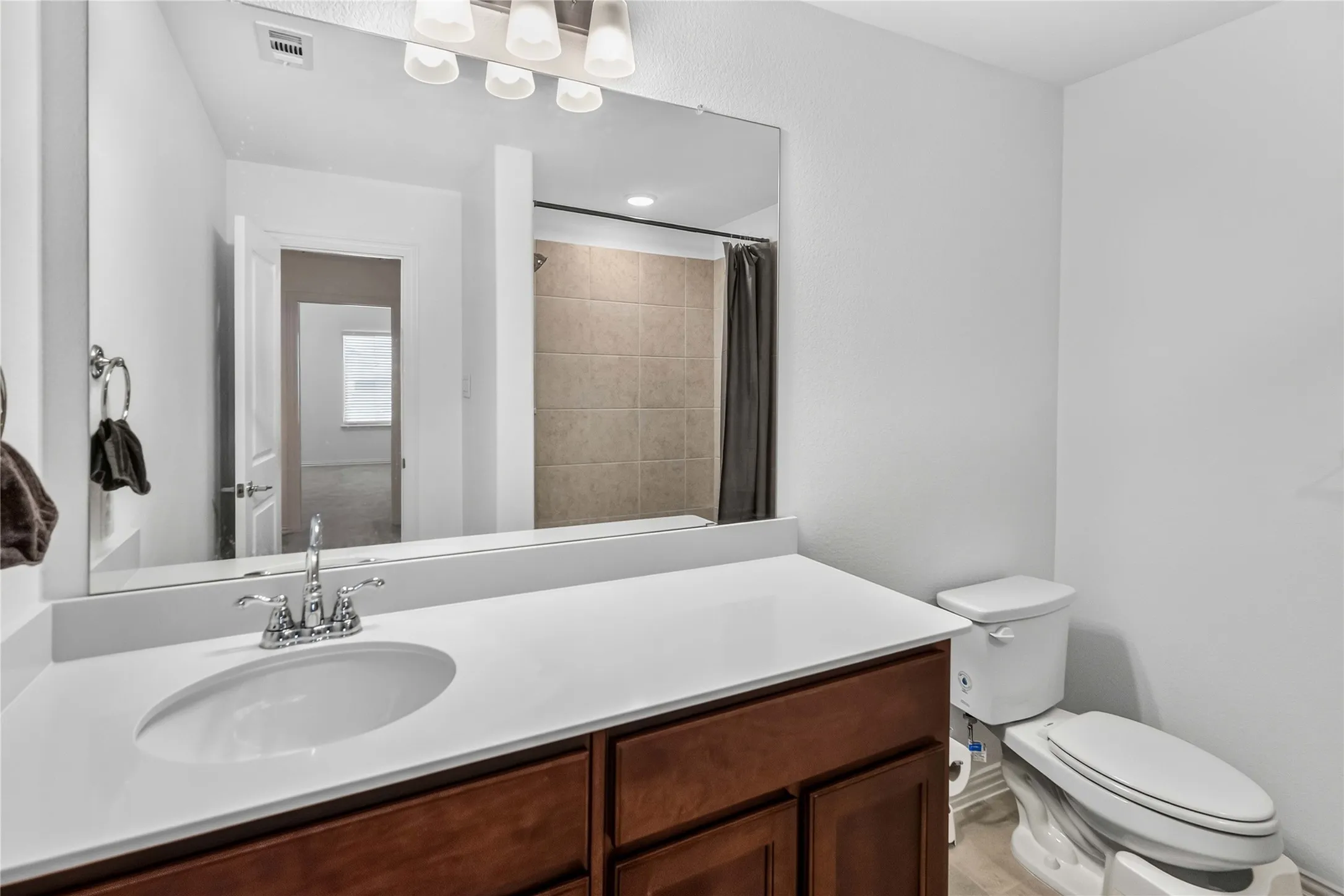Spa-inspired bathroom featuring a wood-finish vanity with dual sinks, white quartz countertop, and chrome fixtures