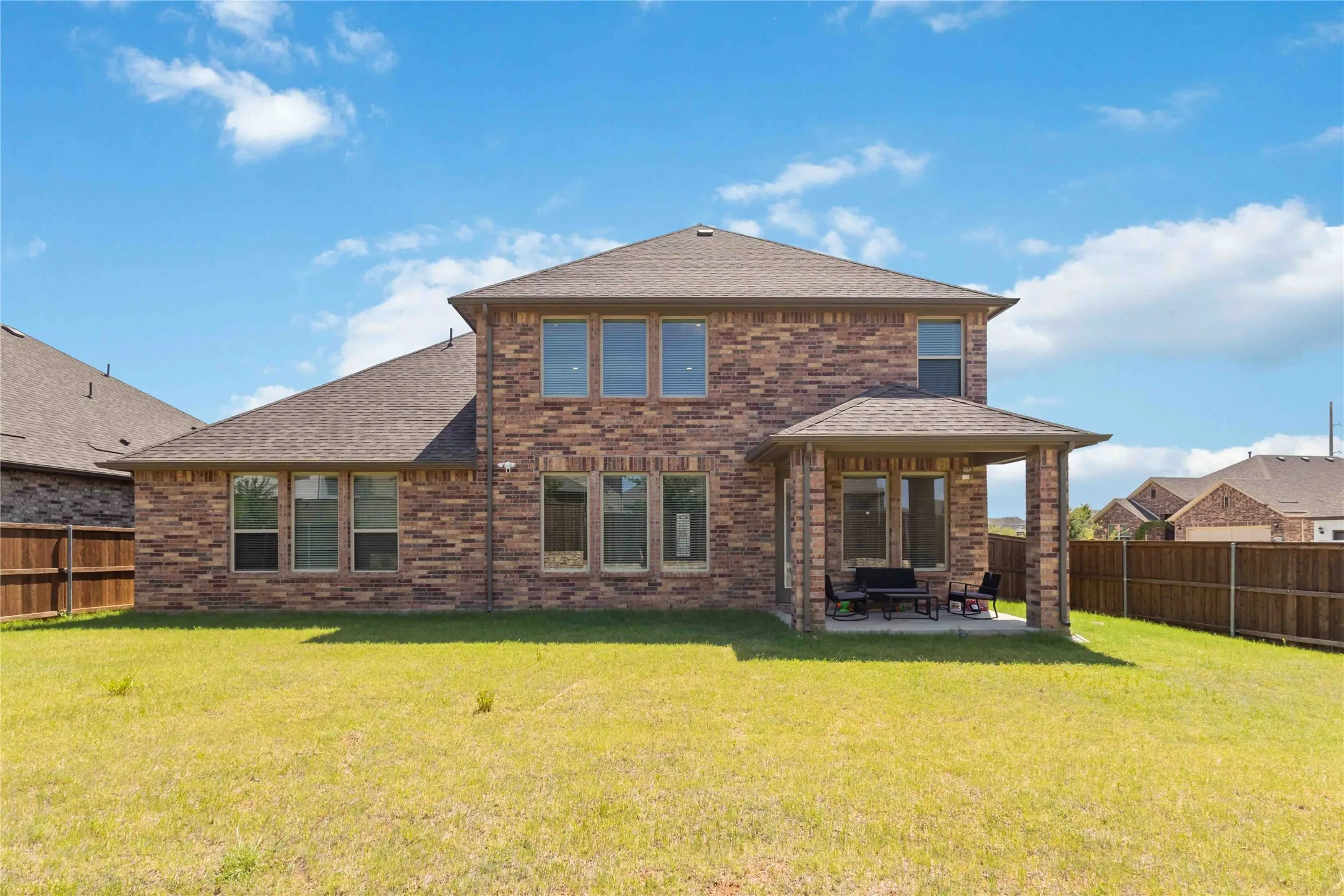 Striking two-story brick home showcasing a spacious rear elevation with covered patio, multiple window banks, and manicured lawn
