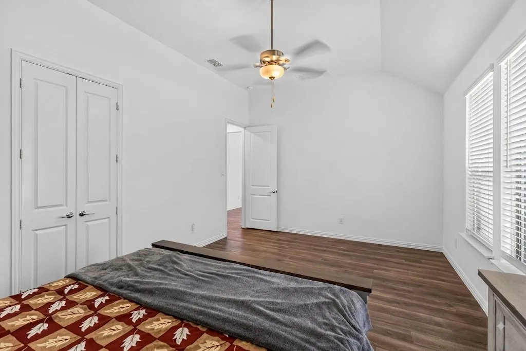 Vaulted ceiling with a ceiling fan, wood-finish flooring, white walls, and a large window with blinds