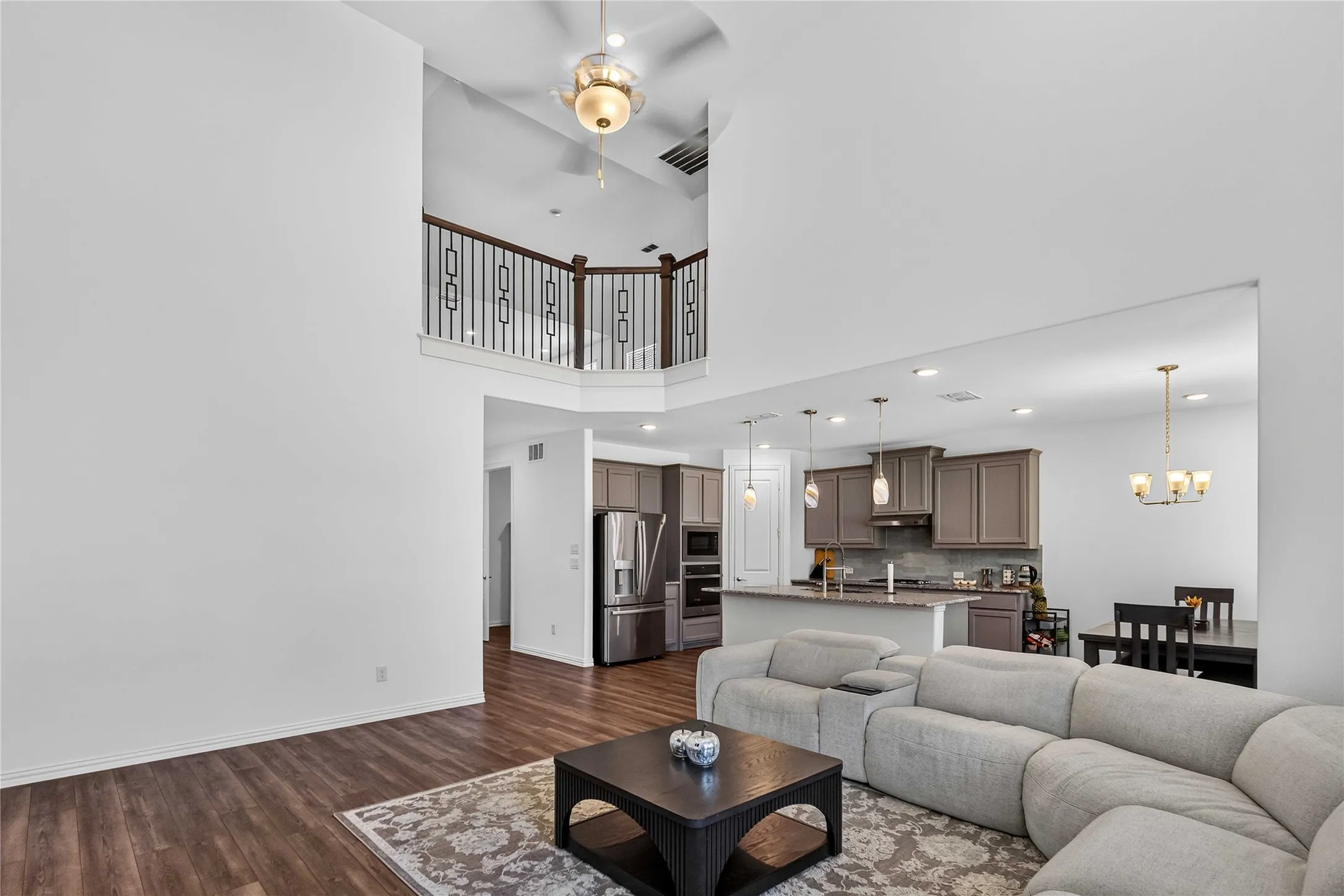 Wood-finish flooring, high ceilings with ceiling fan, second-story railing with decorative balusters, kitchen with pendant lighting, and recessed lighting