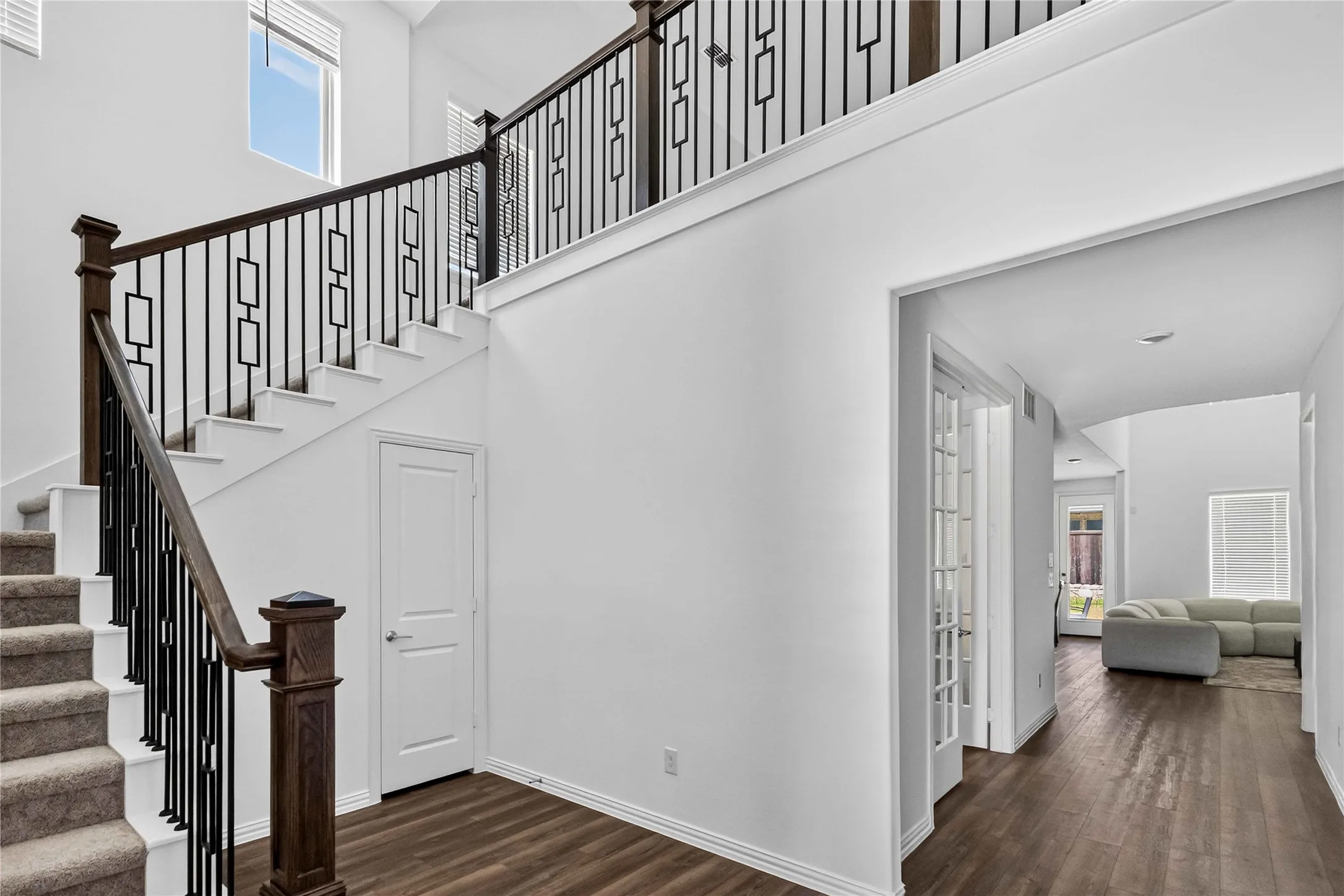 Elegant foyer showcasing a grand staircase with dark wood newel posts and decorative wrought-iron balusters, wide-plank wood-finish flooring, and clean white walls with architectural detail