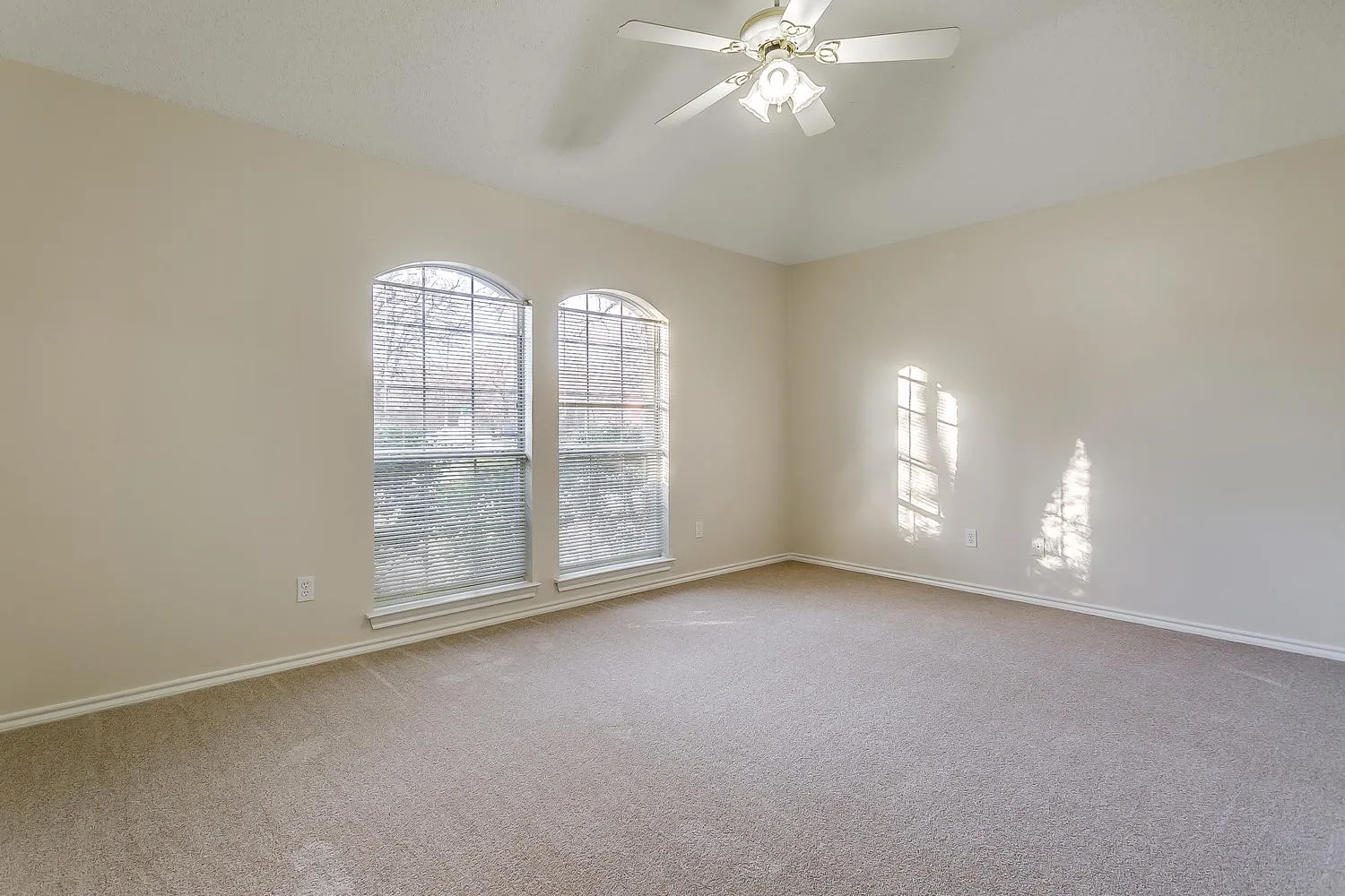 Vaulted ceiling, two arched windows, light-toned carpeting, and a ceiling fan with integrated lighting