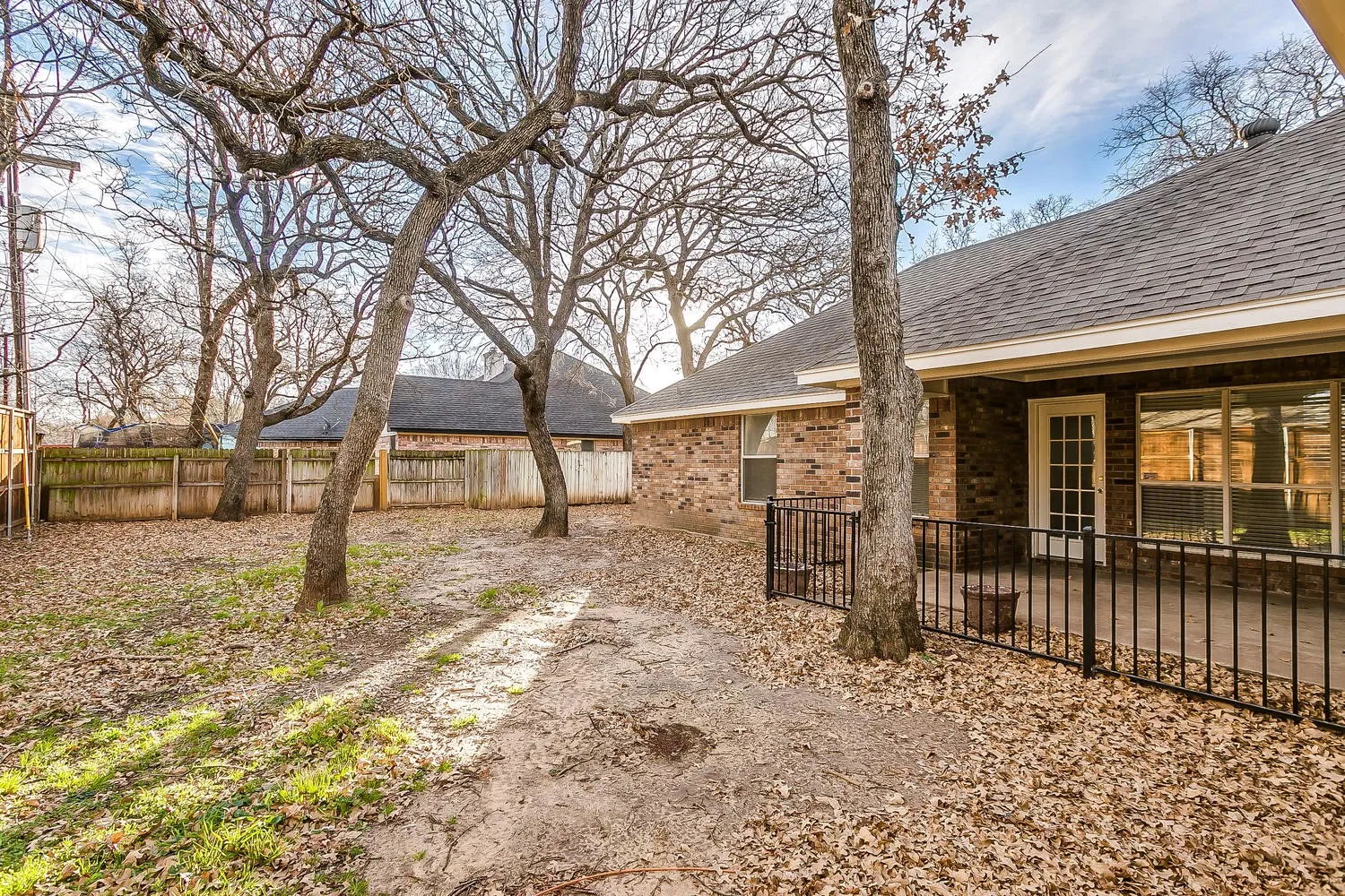 Spacious backyard oasis featuring mature shade trees, gravel hardscaping, and a covered patio with black metal railings
