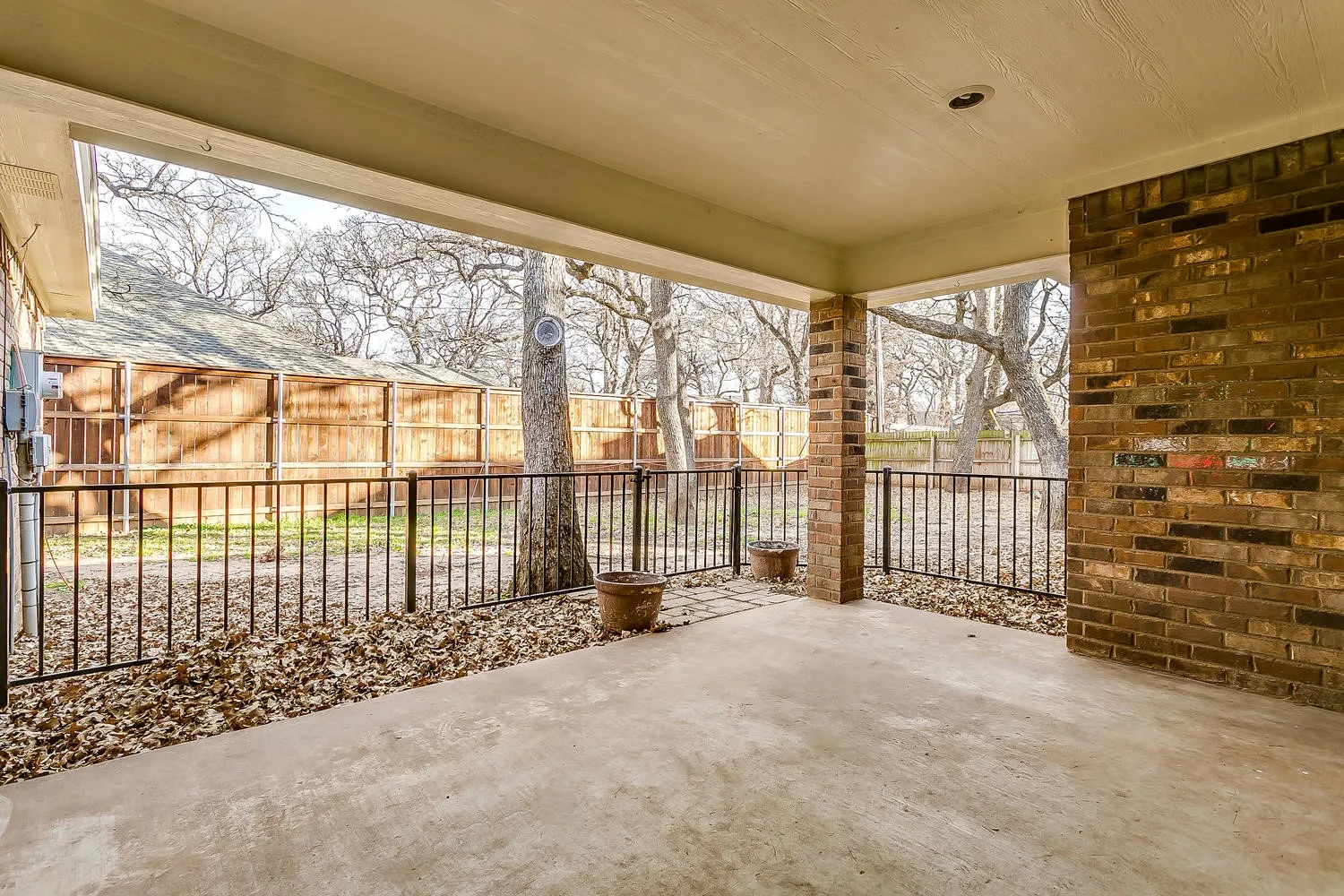 Covered patio with a concrete surface, exposed brick wall, recessed lighting, and black metal railing