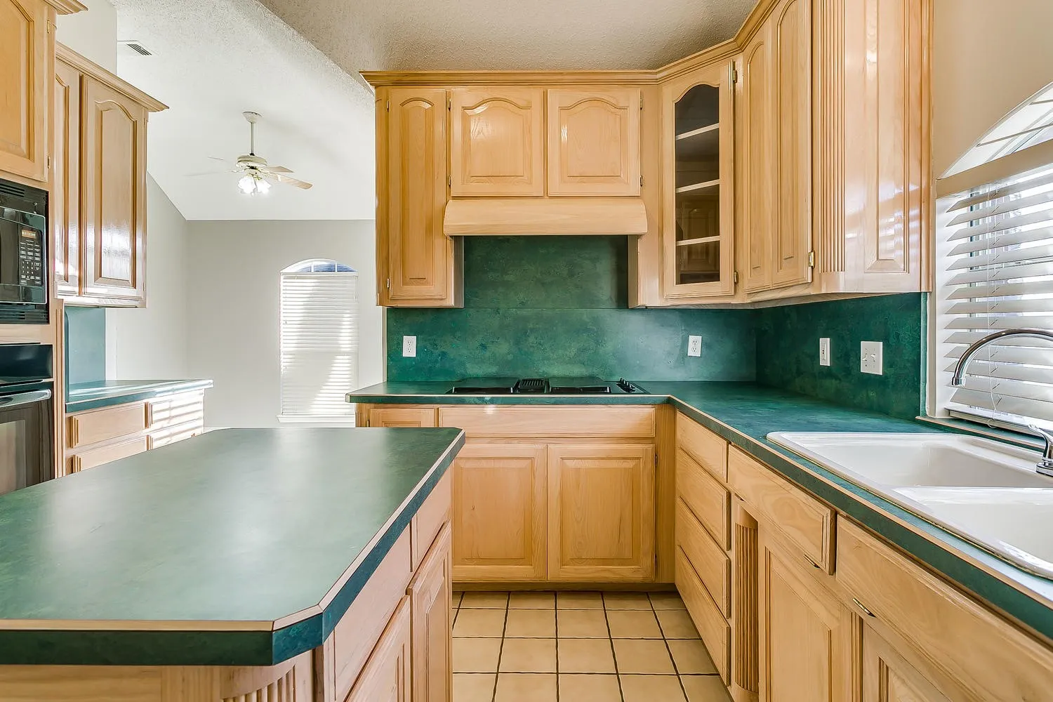 Galley kitchen featuring natural wood cabinetry, deep green tile backsplash, and coordinating solid surface countertops with rounded edges