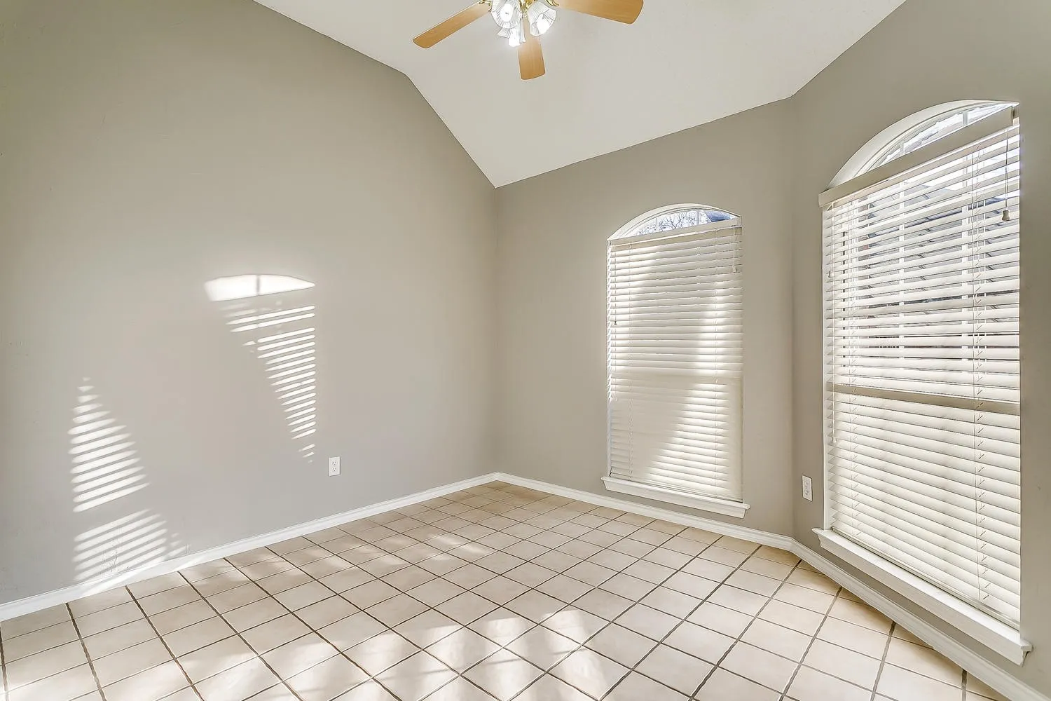 Vaulted ceiling with a ceiling fan, arched windows, tile flooring, and neutral wall tones
